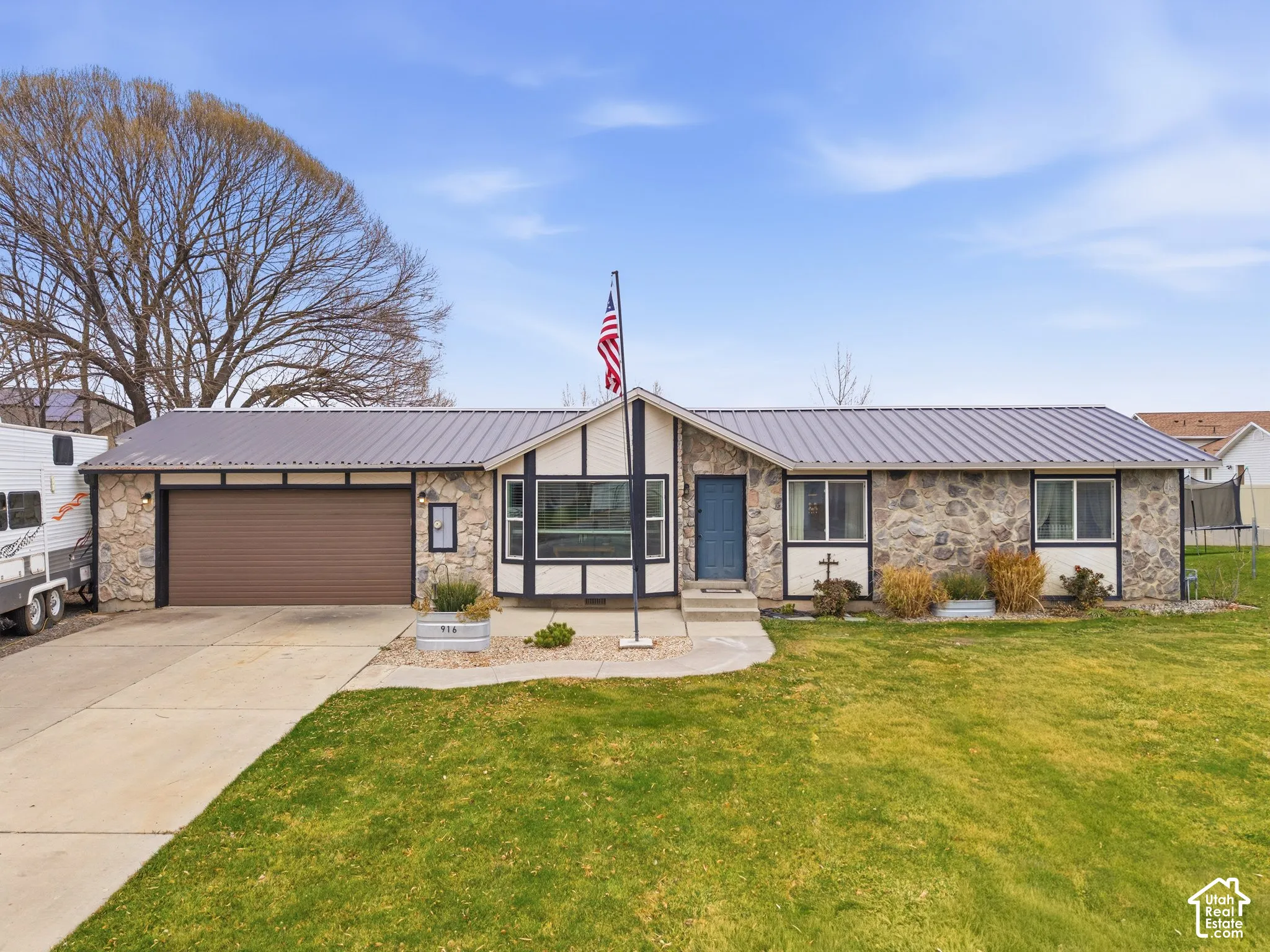 Rambler-style exterior featuring stone veneer siding, metal roofing, an attached two-car garage, and a front lawn