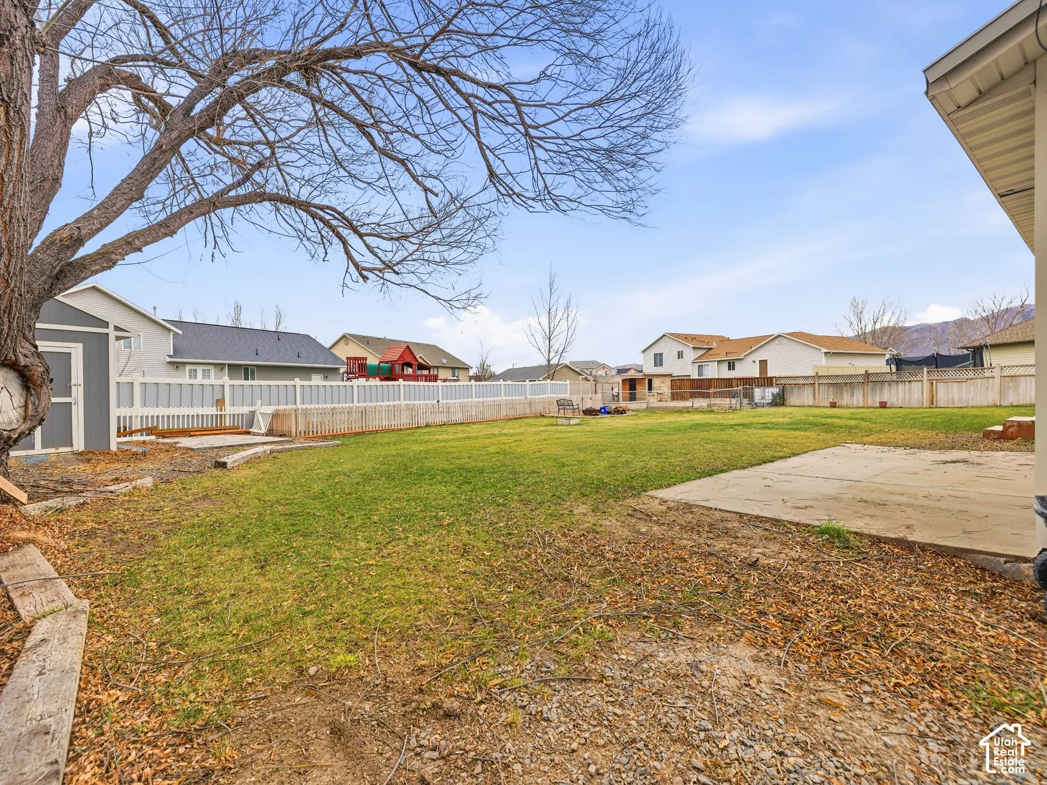 Expansive backyard featuring a concrete patio, perimeter privacy fencing, and a detached storage shed
