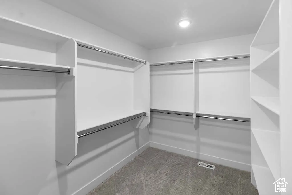 Walk-in closet featuring white built-in shelving, multiple metal hanging rods, and carpeting