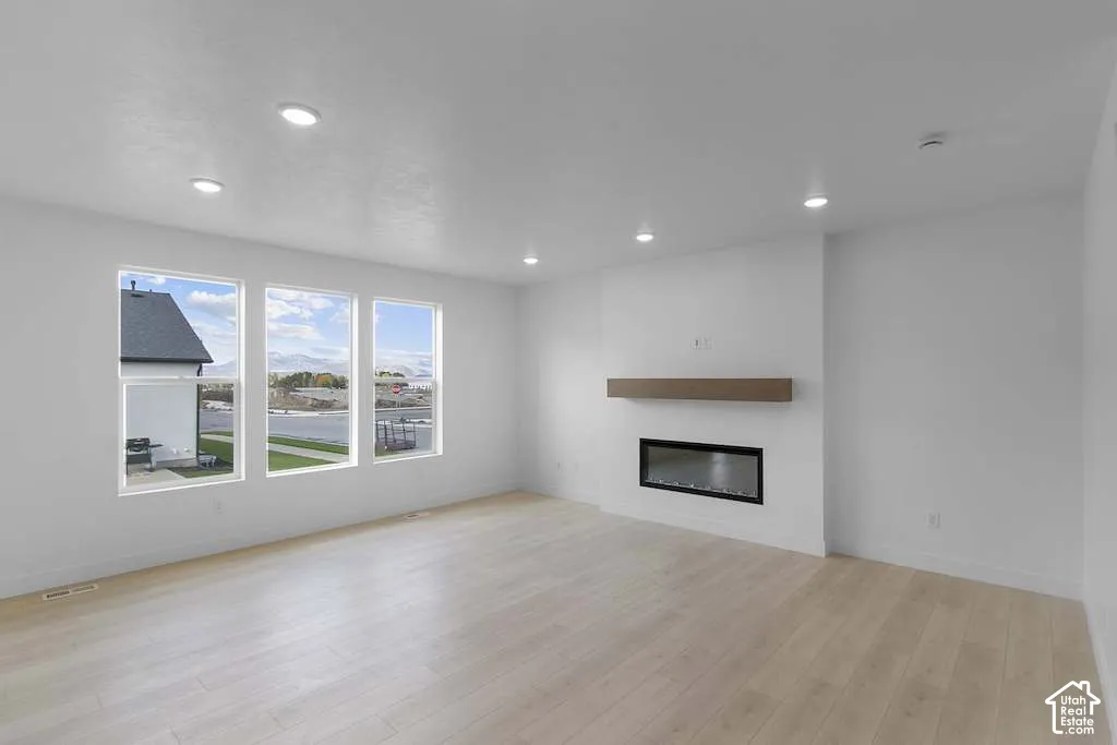 Living area featuring wood-finish flooring, recessed lighting, a horizontal linear fireplace, and a natural wood-finish mantelpiece
