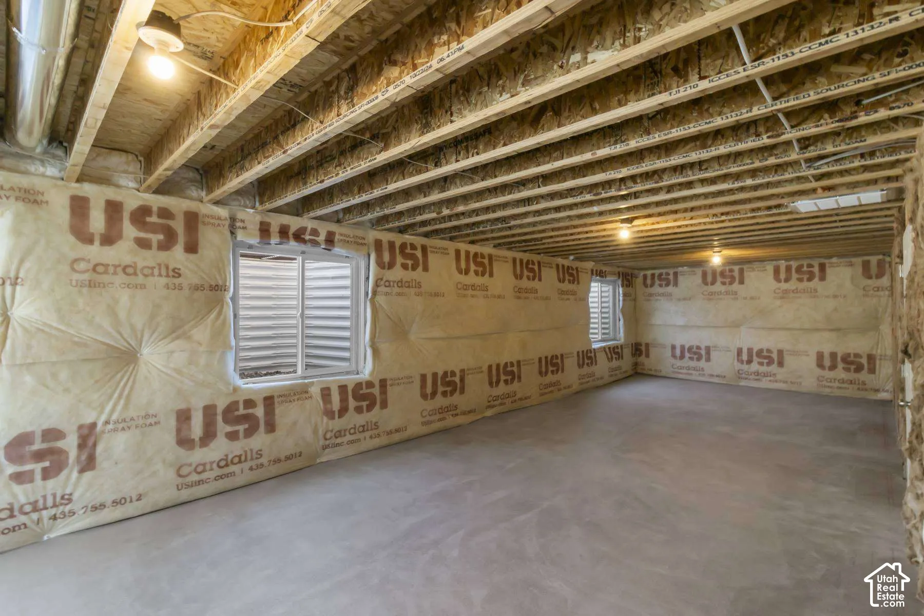 Unfinished space featuring exposed wood-joist ceiling, concrete floor, blanket-style wall insulation, and two sliding windows with window wells
