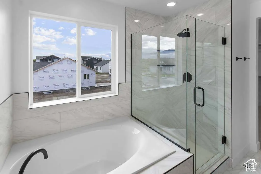Soaking tub with matte black faucet and separate glass-enclosed shower featuring tile surround and matte black hardware