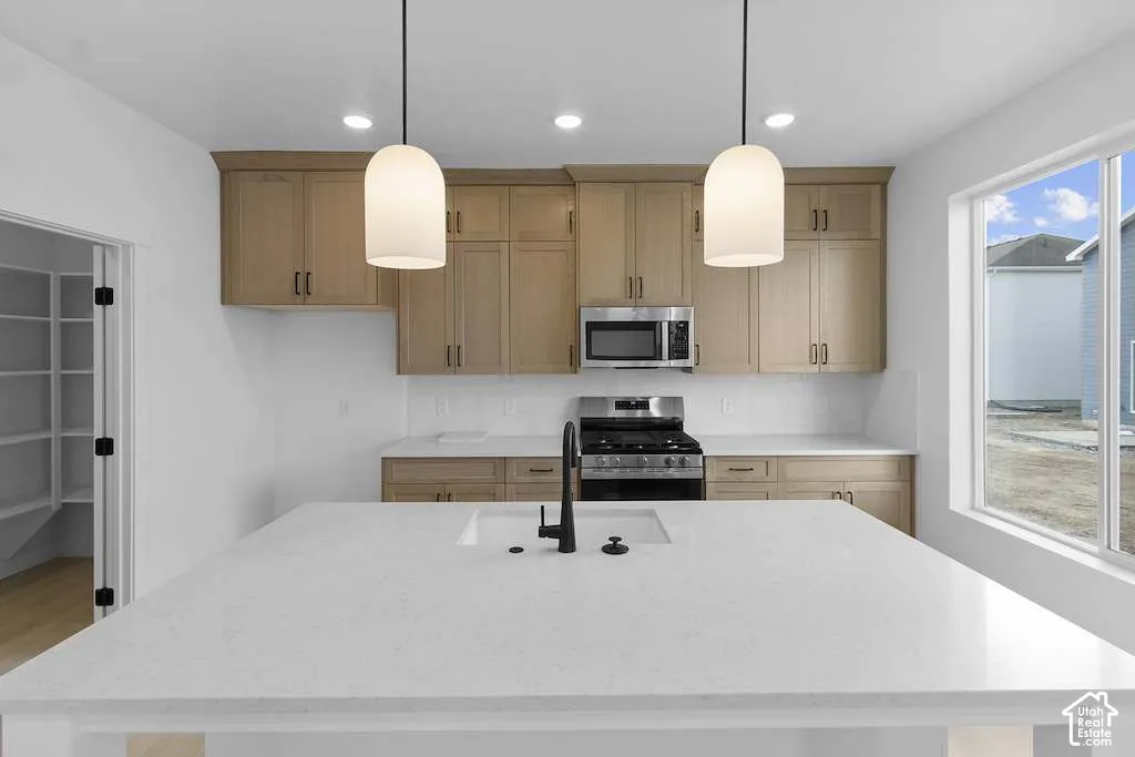 Kitchen featuring light-finish wood cabinetry, a central island with a white countertop and matte black faucet, integrated stainless steel appliances, and dual pendant lighting
