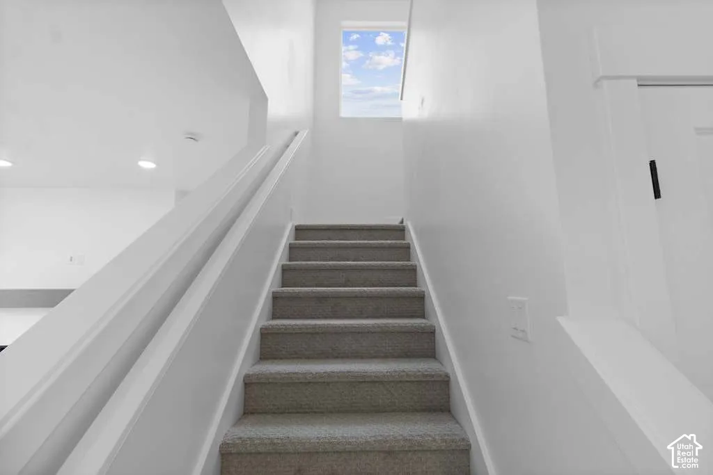 Staircase featuring neutral carpeted treads, white handrails, and a square window providing natural light