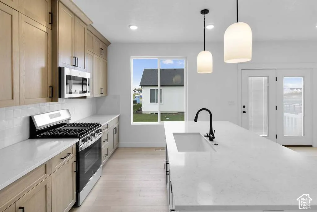 Kitchen featuring light wood-finish cabinetry, quartz countertops, a central island with an undermount sink and matte black faucet, and stainless steel appliances