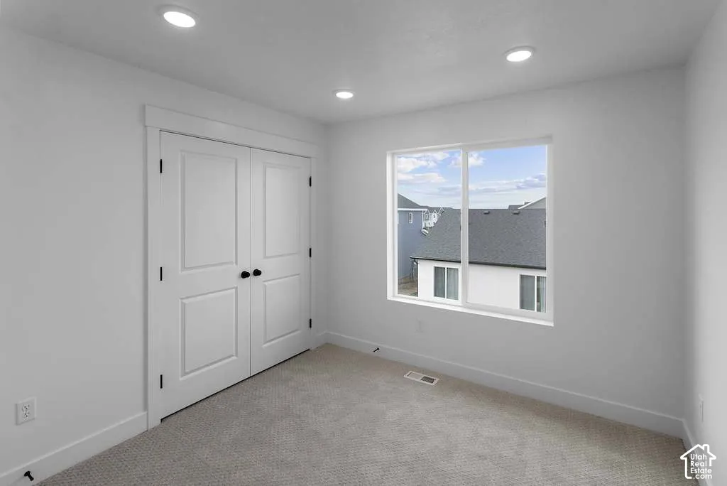 Neutral-toned carpet, recessed ceiling lighting, double-panel closet doors with matte black hardware, and a large slider window