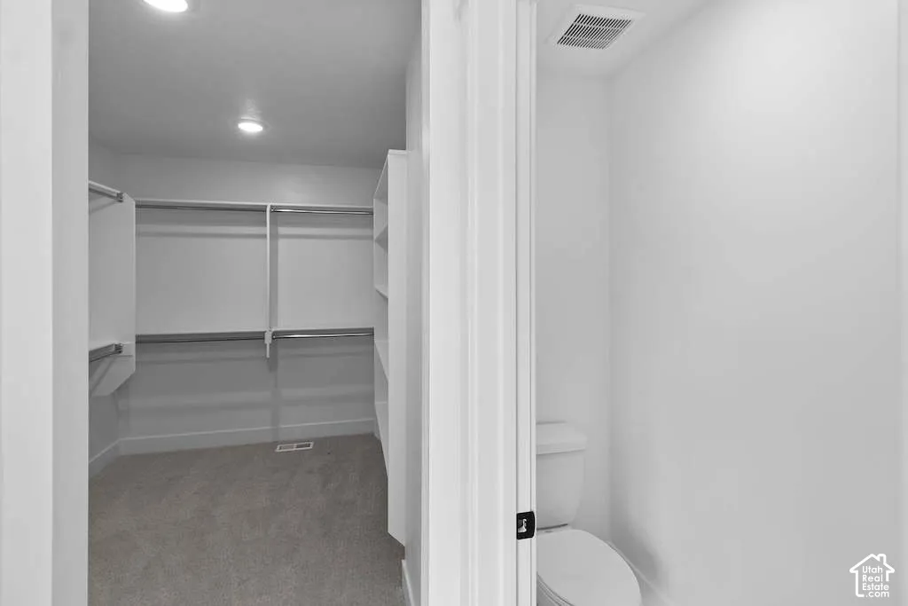Walk-in closet featuring white tiered shelving and metal clothing rods, paired with a water closet containing a white porcelain toilet