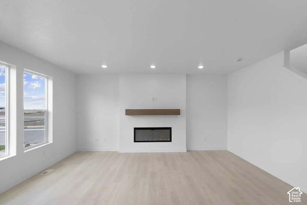 Recessed lighting, wood-finish flooring, and a linear electric fireplace featuring a mounted wood-tone mantel