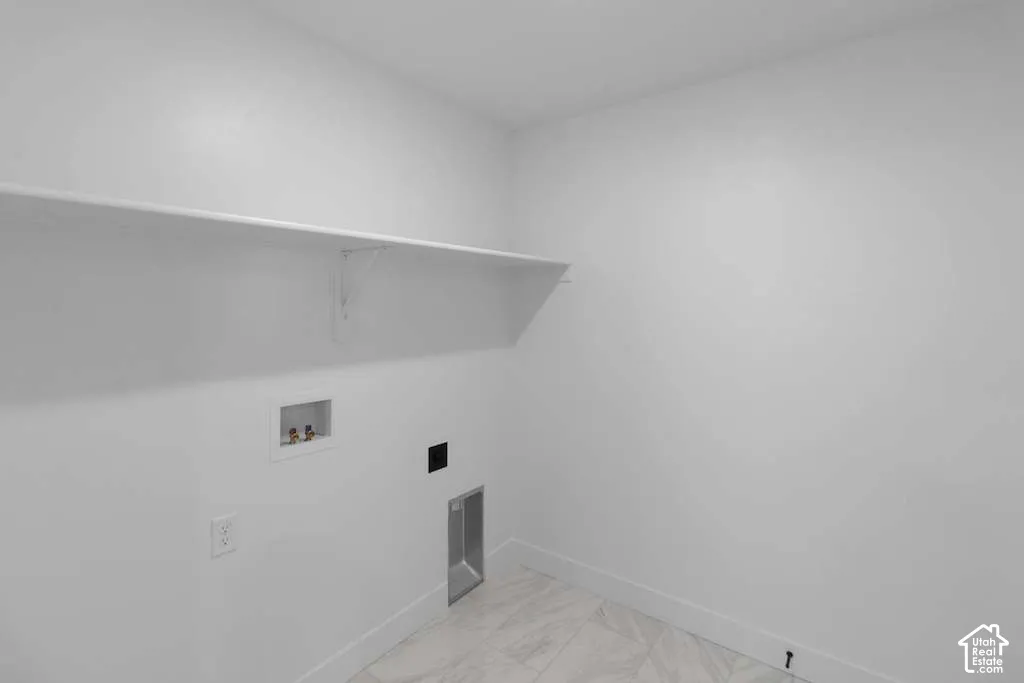Utility space featuring white walls, stone-finish flooring, a wall-mounted shelf, and dedicated water and electrical hookups
