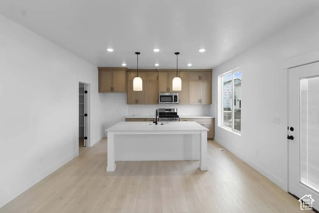 Kitchen featuring light wood-finish cabinetry, a white central island, stainless steel appliances, recessed ceiling lighting, and wood-finish flooring