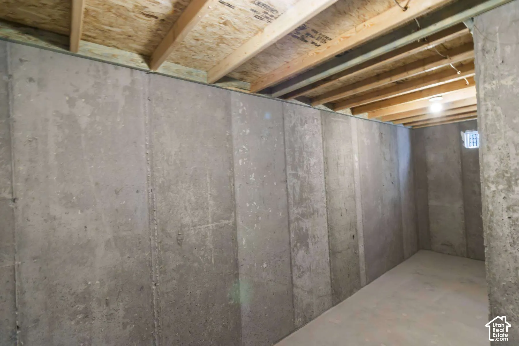 Unfinished utility space featuring poured concrete walls, exposed wood ceiling joists, and a concrete floor
