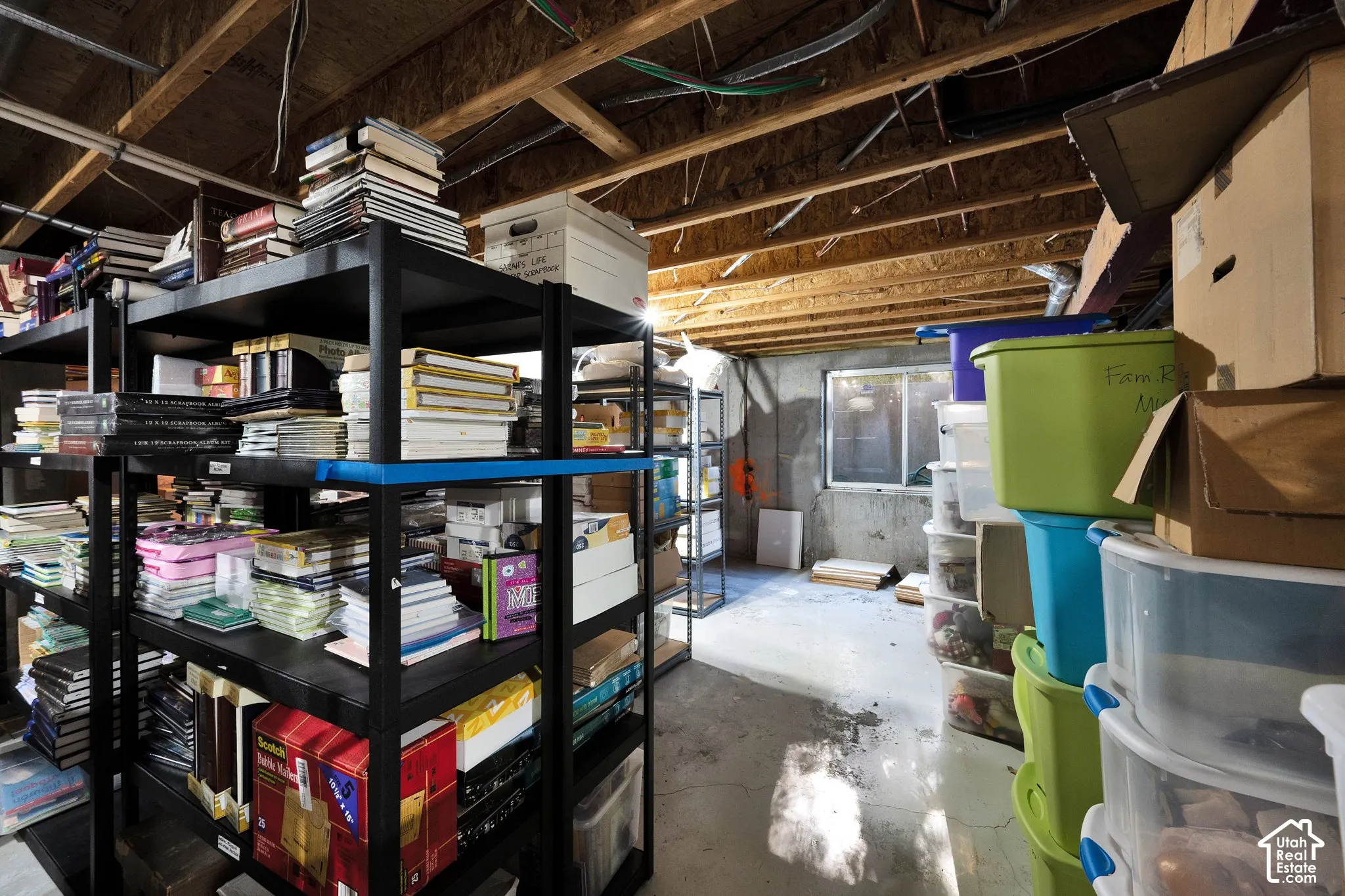 Unfinished lower-level storage area featuring exposed wood-joist ceiling, concrete walls, painted concrete flooring, and a sliding window