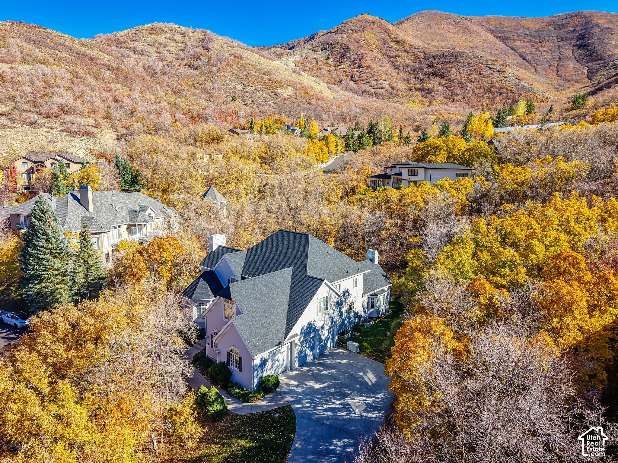Multi-gabled roofline with asphalt shingles, stone chimney stacks, and expansive mountain backdrop featuring mature autumn foliage