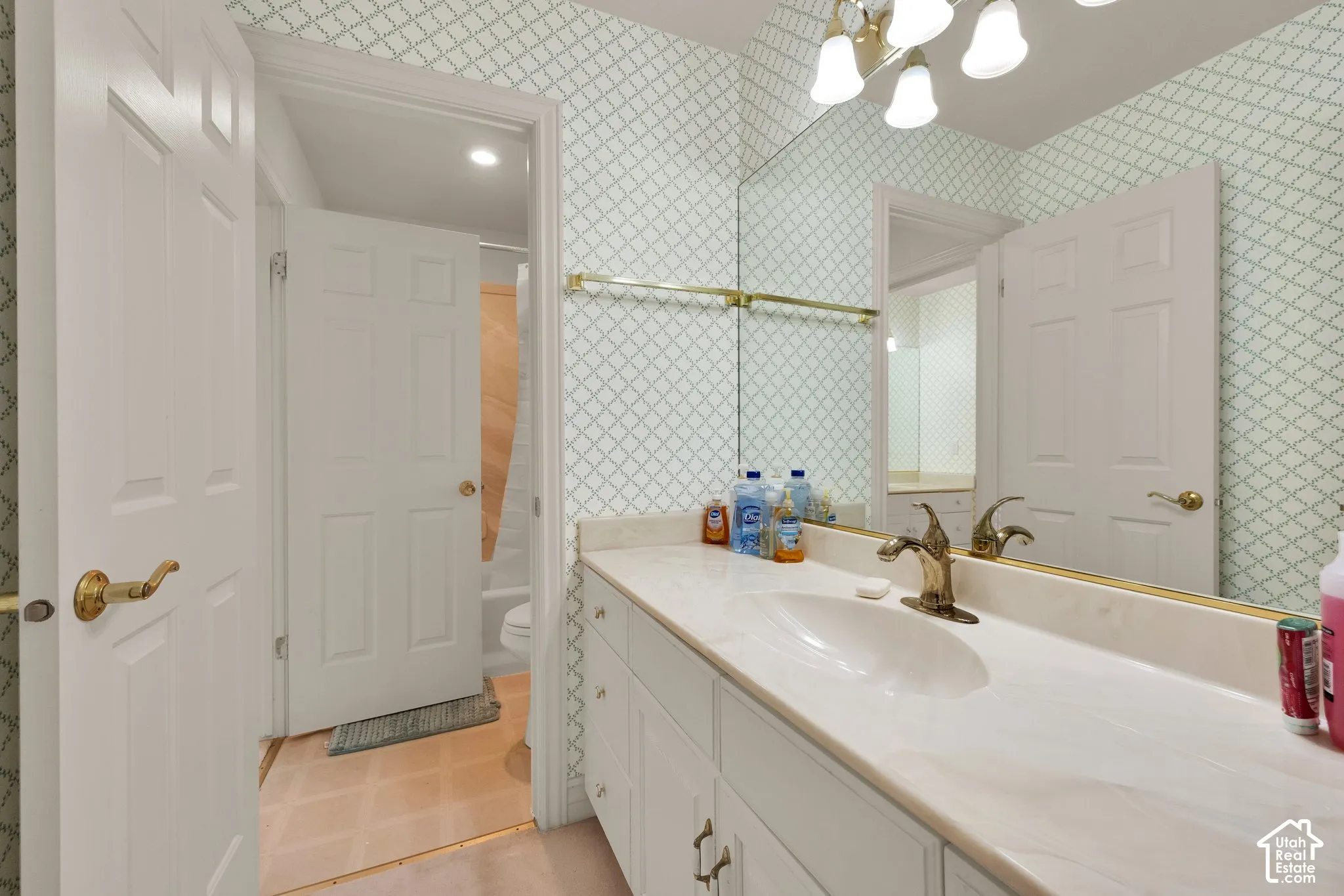 Bathroom featuring white cabinetry, integrated sink, polished metal hardware, full-width wall mirror, and five-light vanity fixture