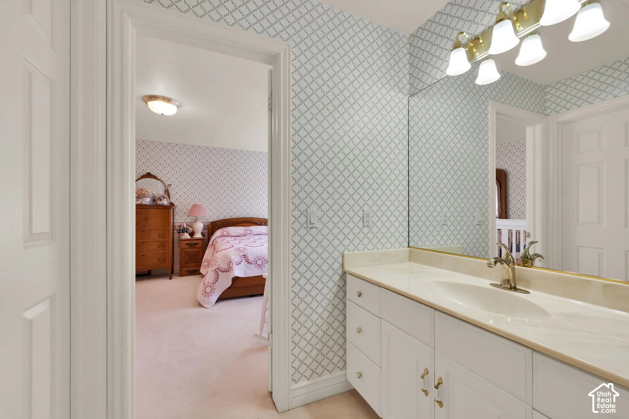 Bathroom featuring white cabinetry, integrated sink, expansive vanity mirror, and multi-bulb wall lighting