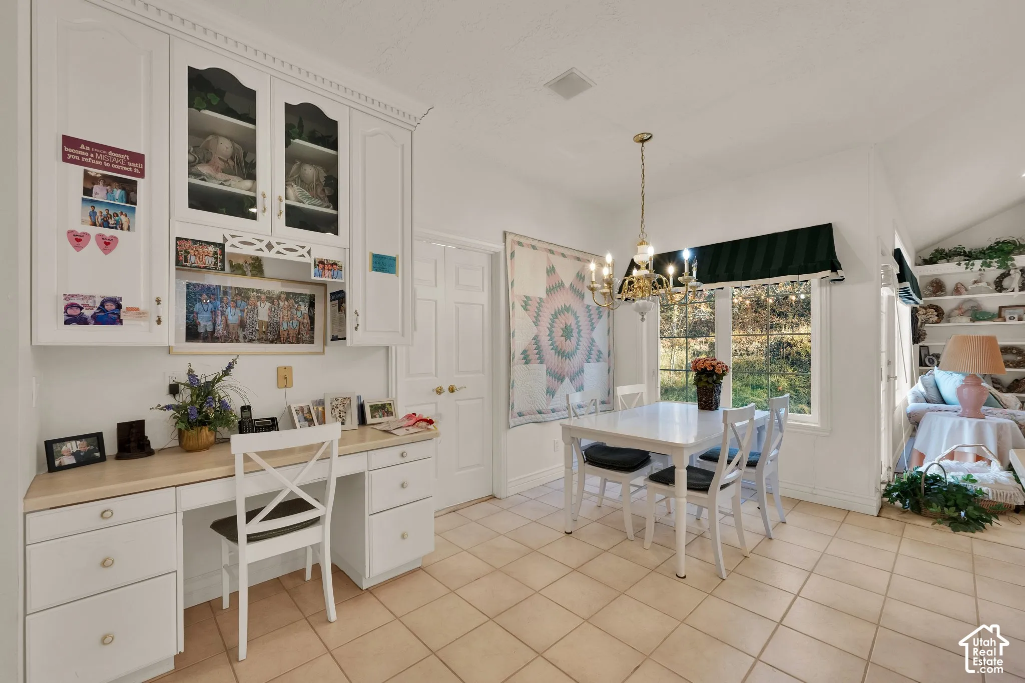 White custom built-in cabinetry, integrated desk workspace, ceramic tile flooring, multi-pane window, and classic chandelier lighting