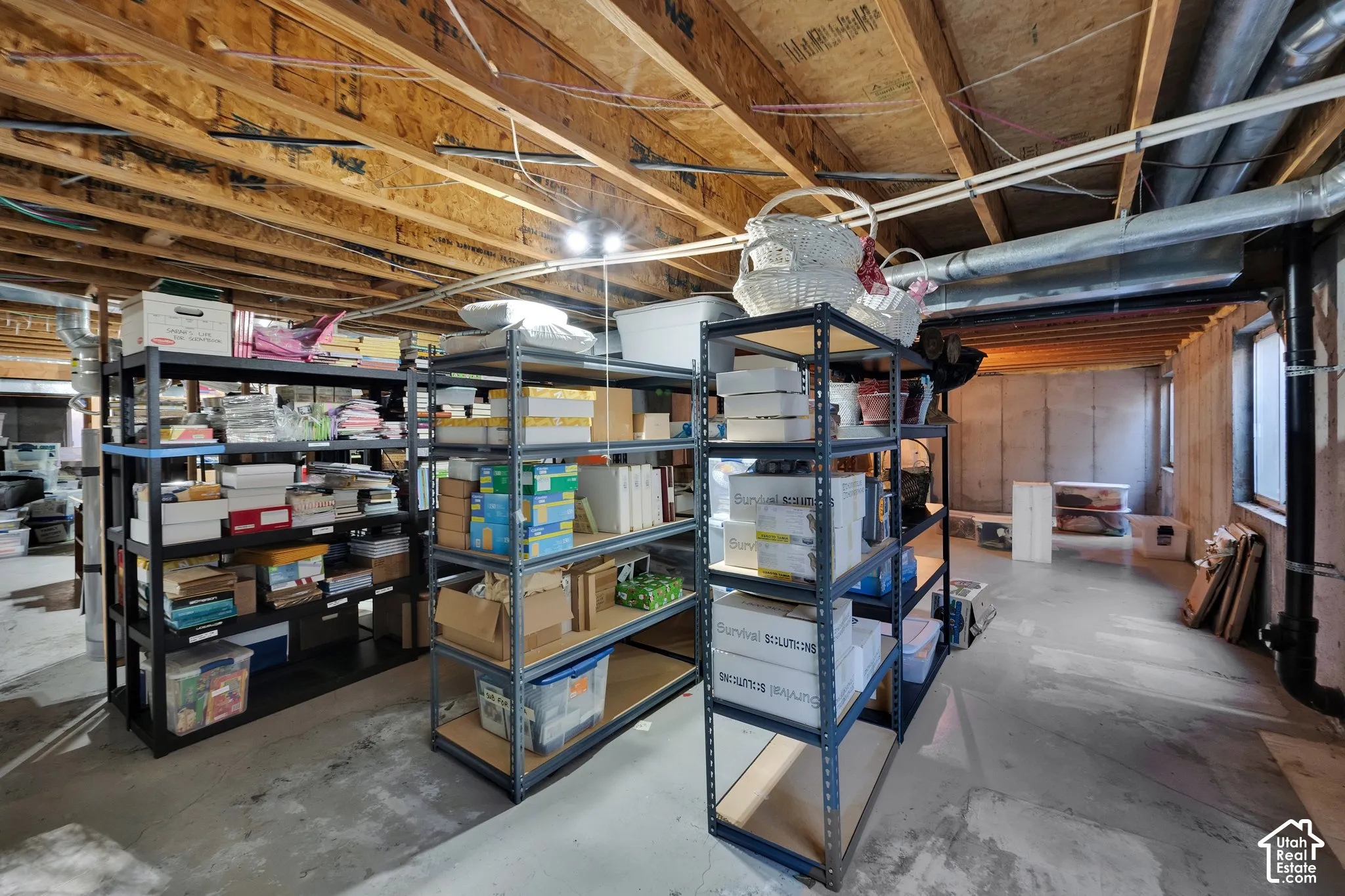 Unfinished basement space featuring exposed wooden floor joists, concrete flooring, and a window