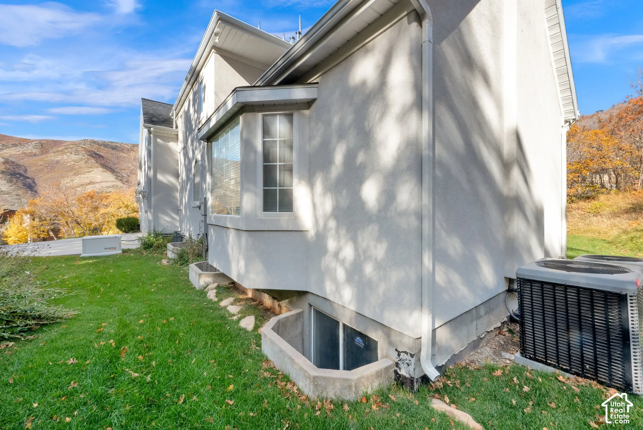 Exterior facade featuring a smooth stucco finish, bay window, window well, and mountainous backdrop