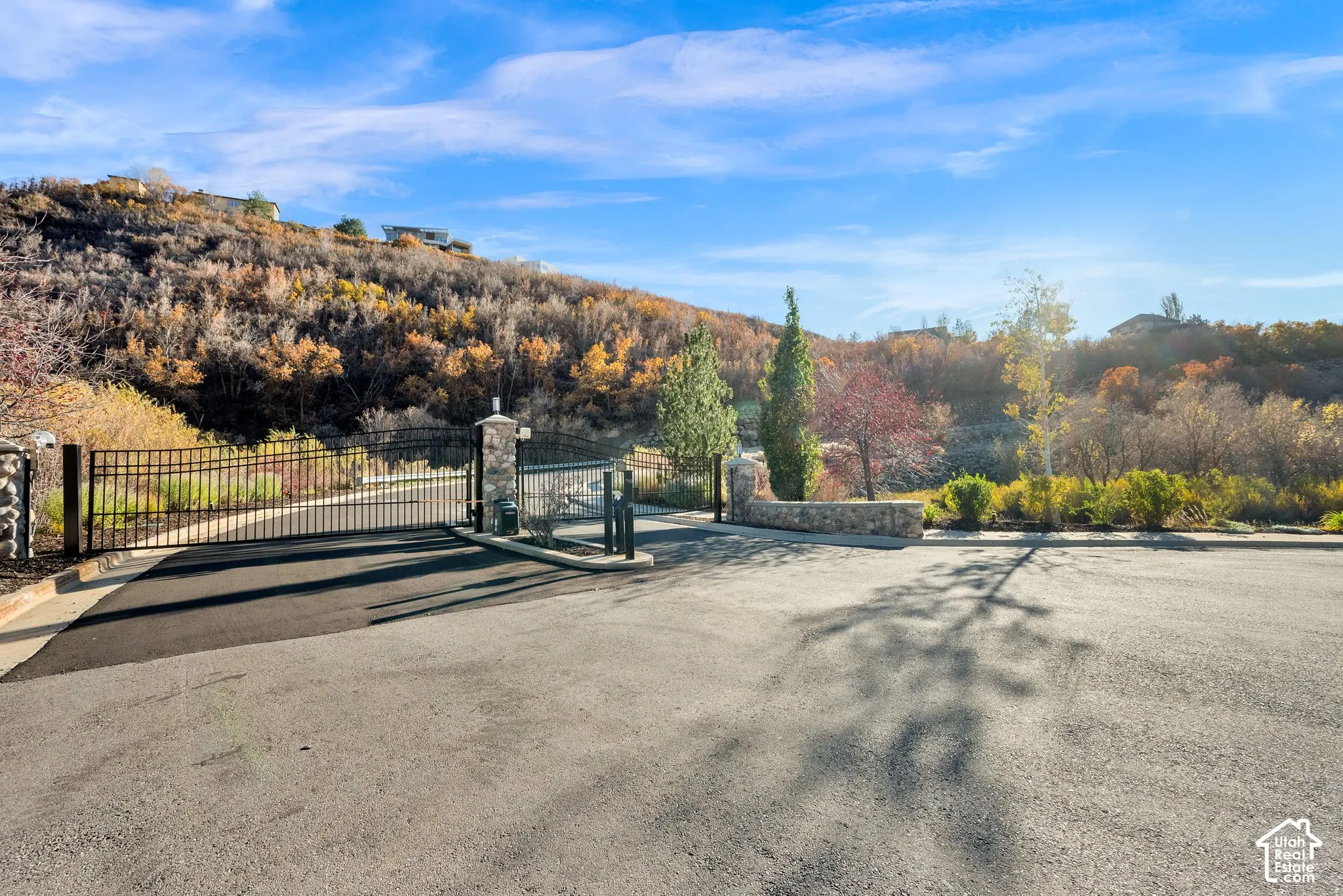 Gated entry featuring a custom metal security gate with stone-clad masonry pillars and asphalt paving