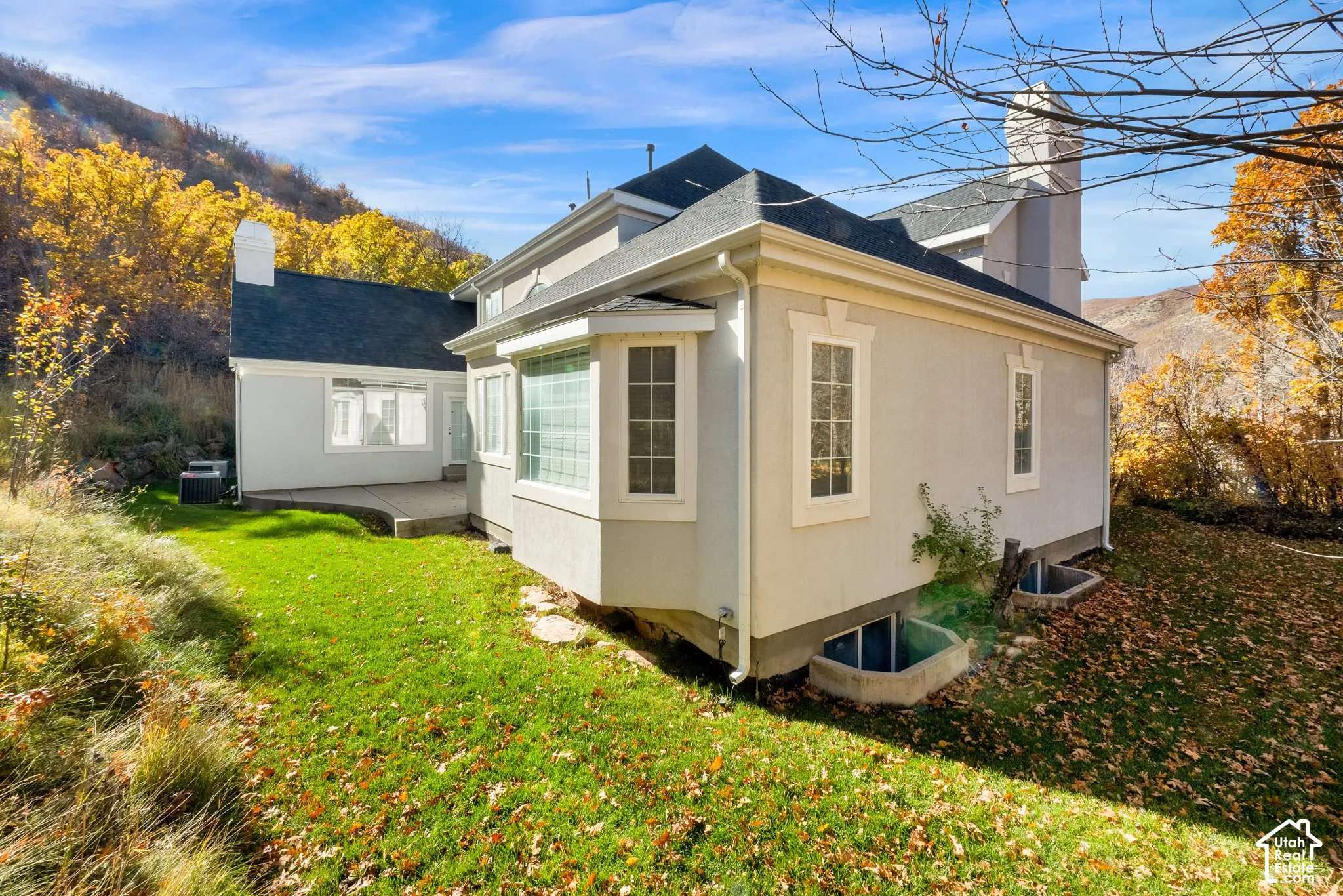 Stucco exterior featuring dual chimneys, a bay window, concrete patio, and subterranean window wells