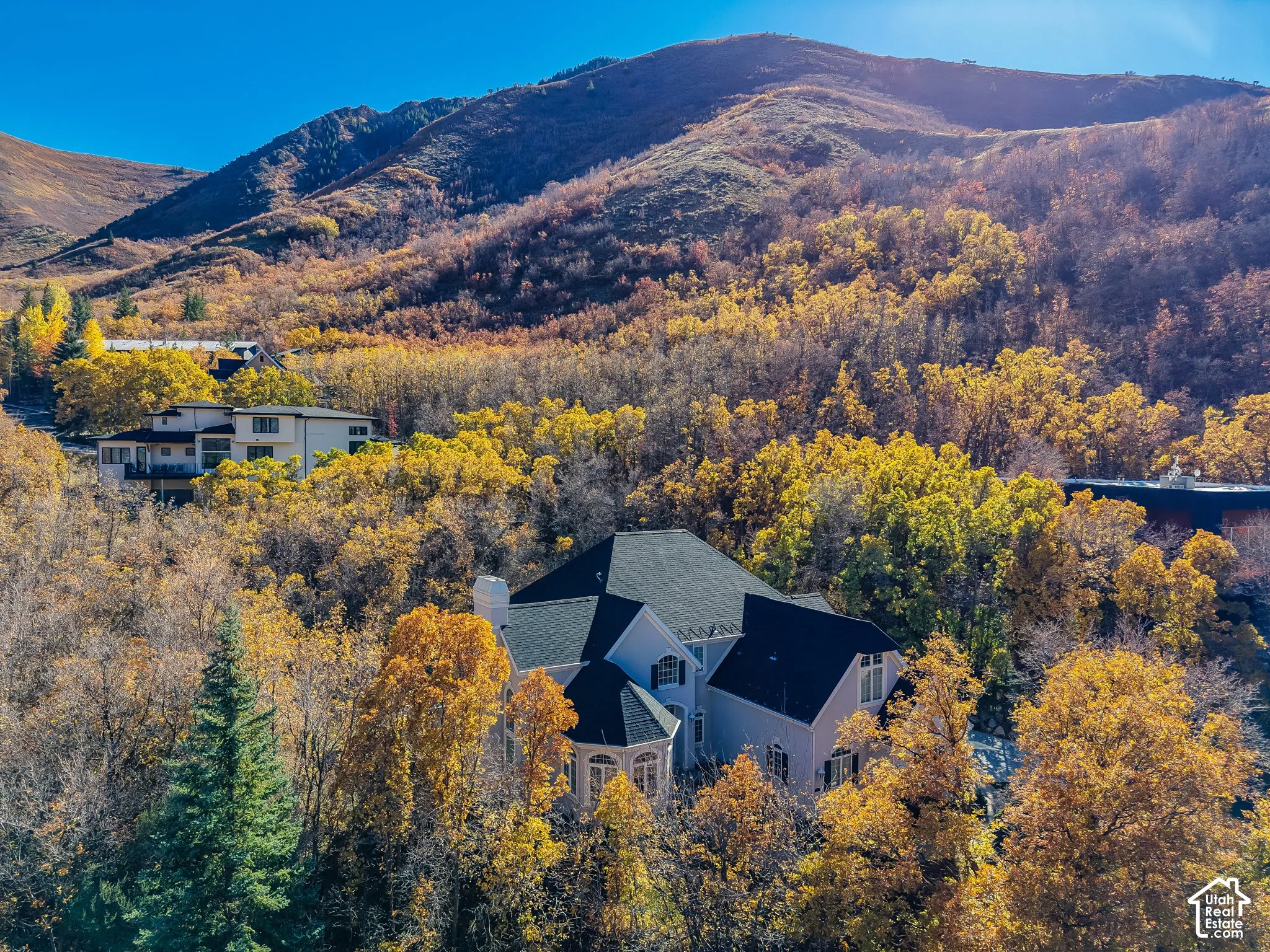 Multi-story residence featuring light-toned stucco siding, a dark shingled roof, a turret-style architectural element, and a mountain backdrop