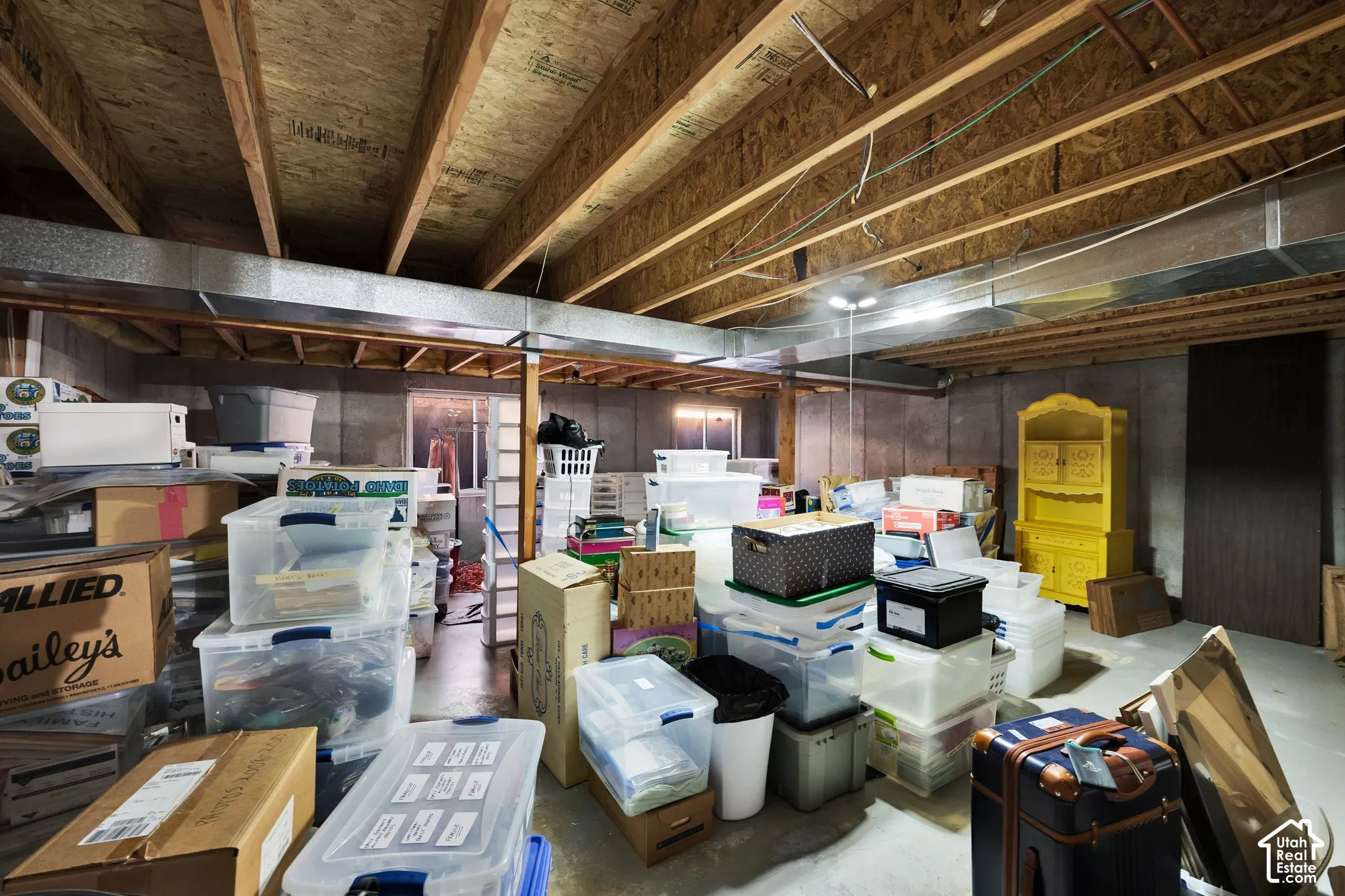 Unfinished basement area with exposed wood ceiling joists, concrete foundation walls, and two egress-style windows