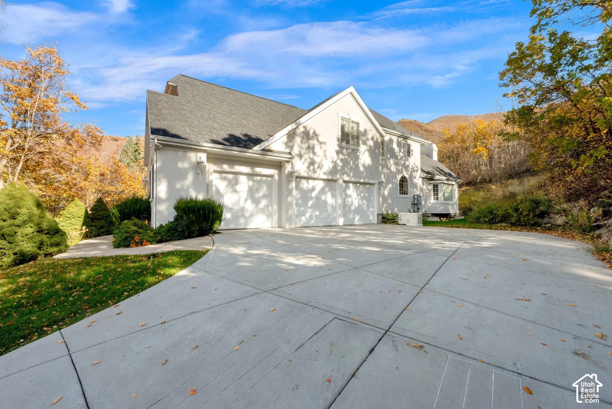 Stucco exterior residence featuring an expansive concrete driveway, a three-car garage, gable rooflines, and a mountain backdrop