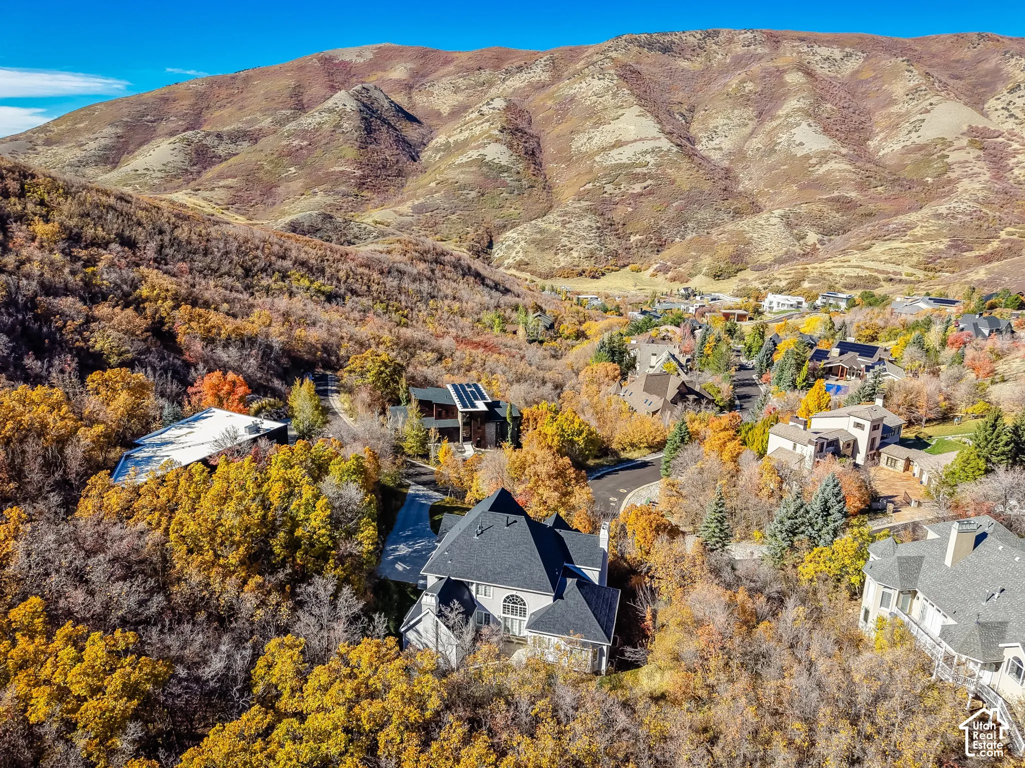 Aerial perspective featuring multi-level architecture with shingled roofing, set against a backdrop of mountainous terrain and mature deciduous foliage