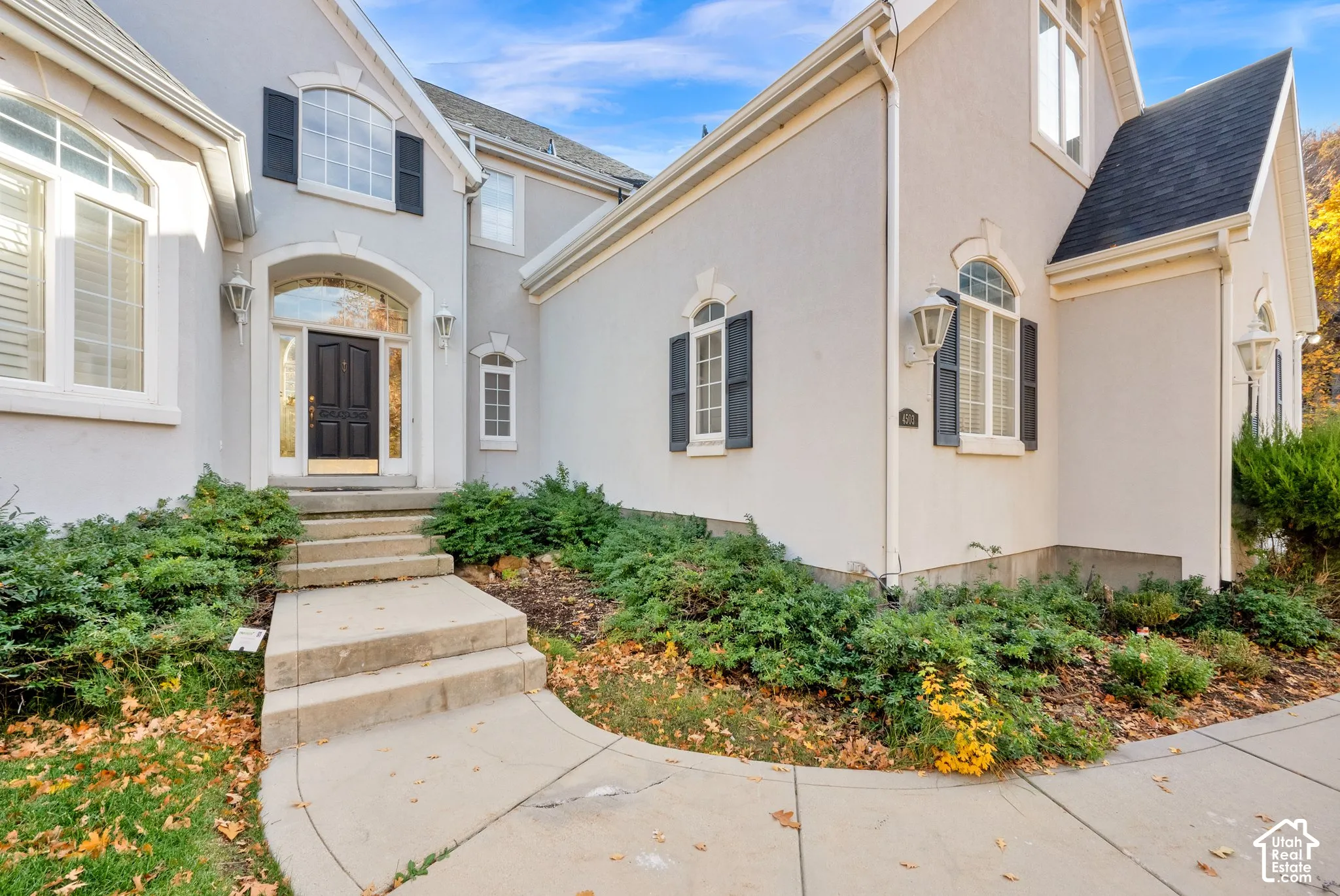 Stucco exterior featuring arched windows, decorative shutters, a covered entryway with a transom window, and a concrete walkway