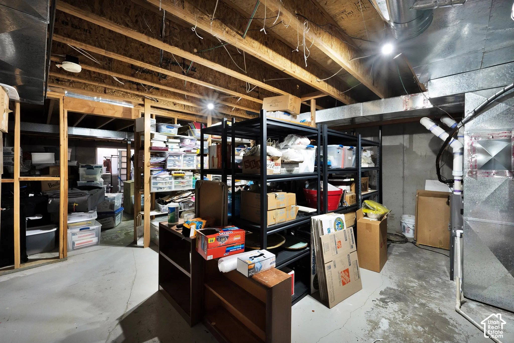 Unfinished storage area featuring exposed wood ceiling joists, concrete flooring, and exposed metal ductwork