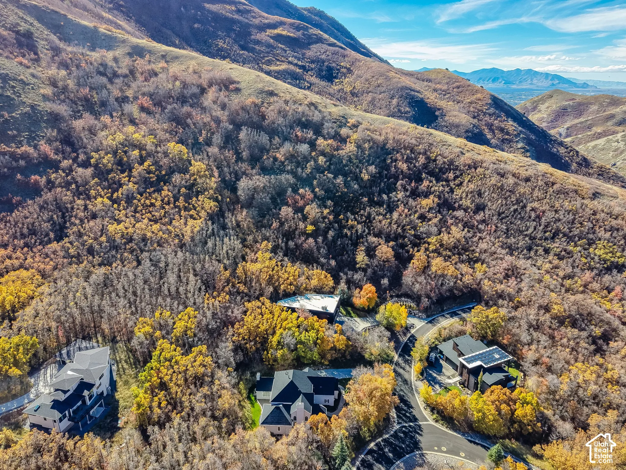 Aerial perspective of a hillside residential development featuring custom architectural homes, paved cul-de-sac infrastructure, and immediate access to mountainous terrain with mature native vegetation