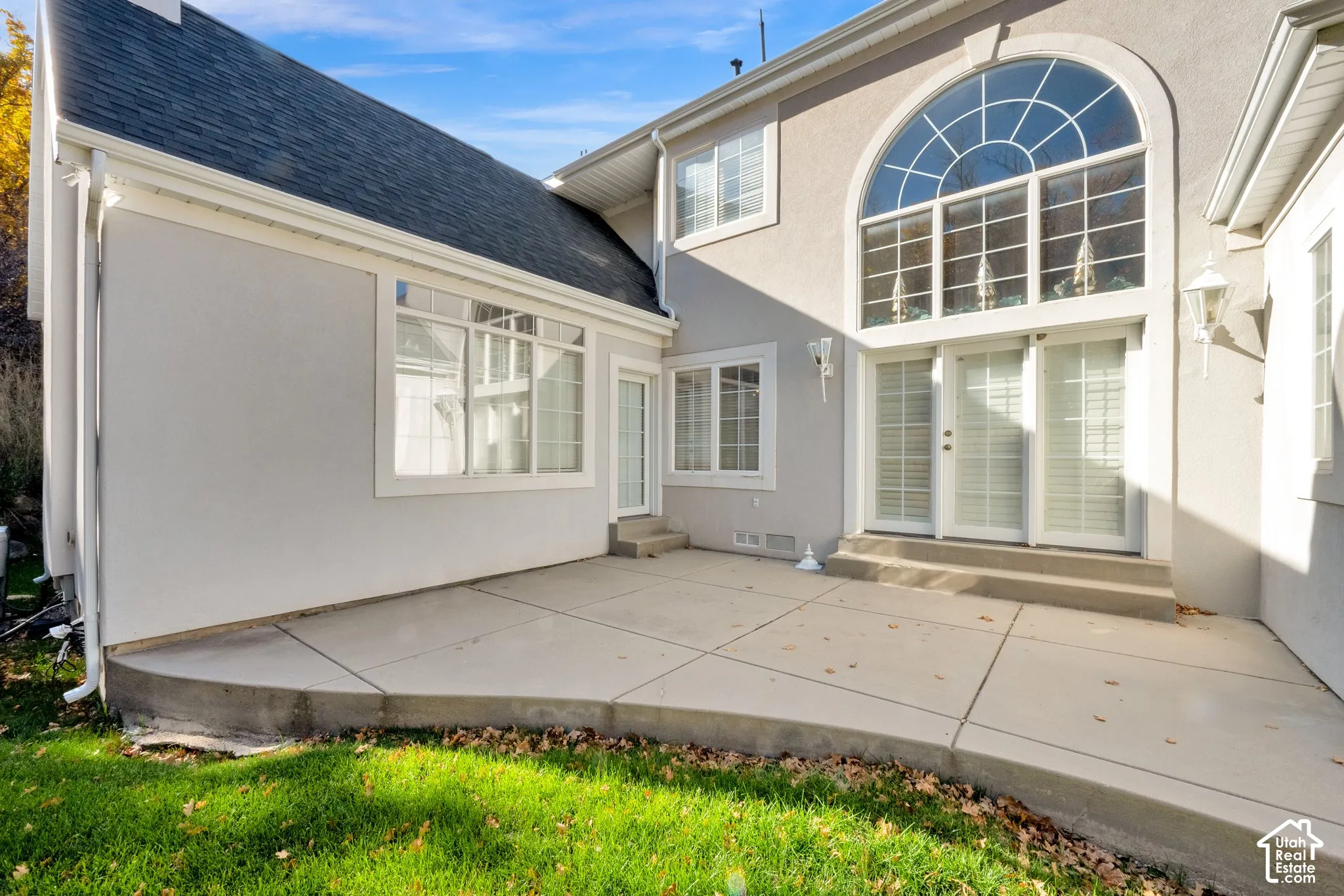Stucco exterior featuring a concrete patio, an expansive arched window, grid-patterned glass doors, and a multi-pitched shingled roof