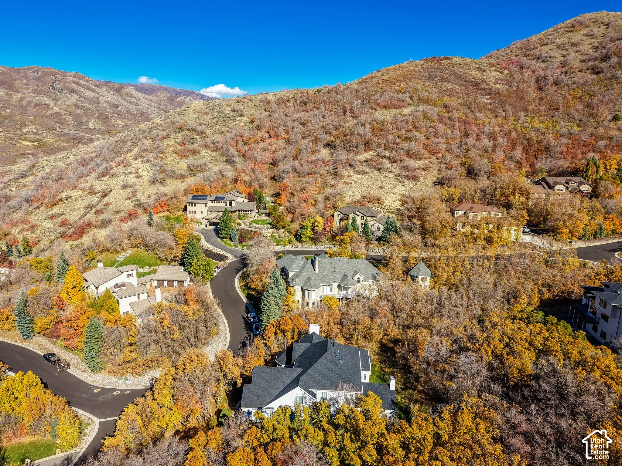 Aerial perspective of a hillside residential community featuring multi-level dwellings, asphalt roads, and mature native vegetation set against a mountainous backdrop