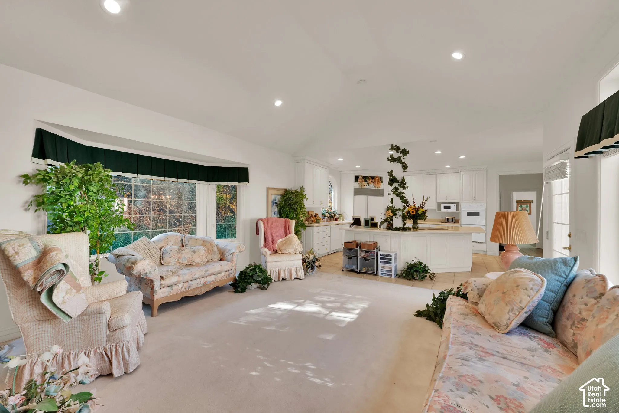 Vaulted ceilings, expansive bay window, recessed lighting, and kitchen island with white cabinetry