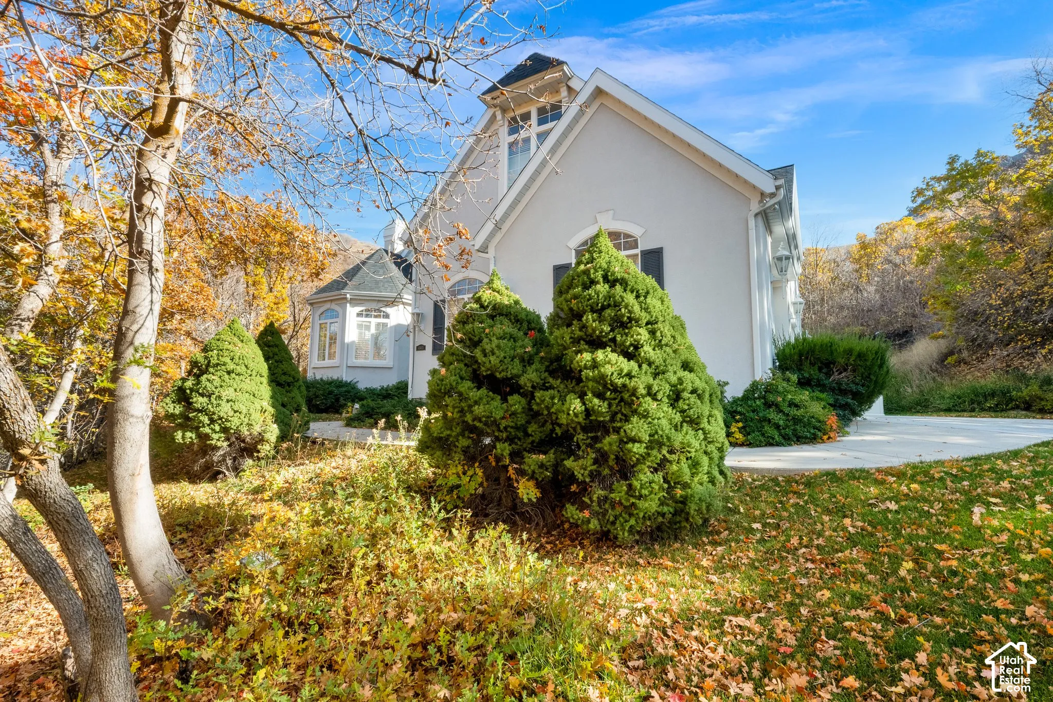 Exterior facade featuring light-toned stucco siding, steep roof gables, arched window detailing, and a concrete patio
