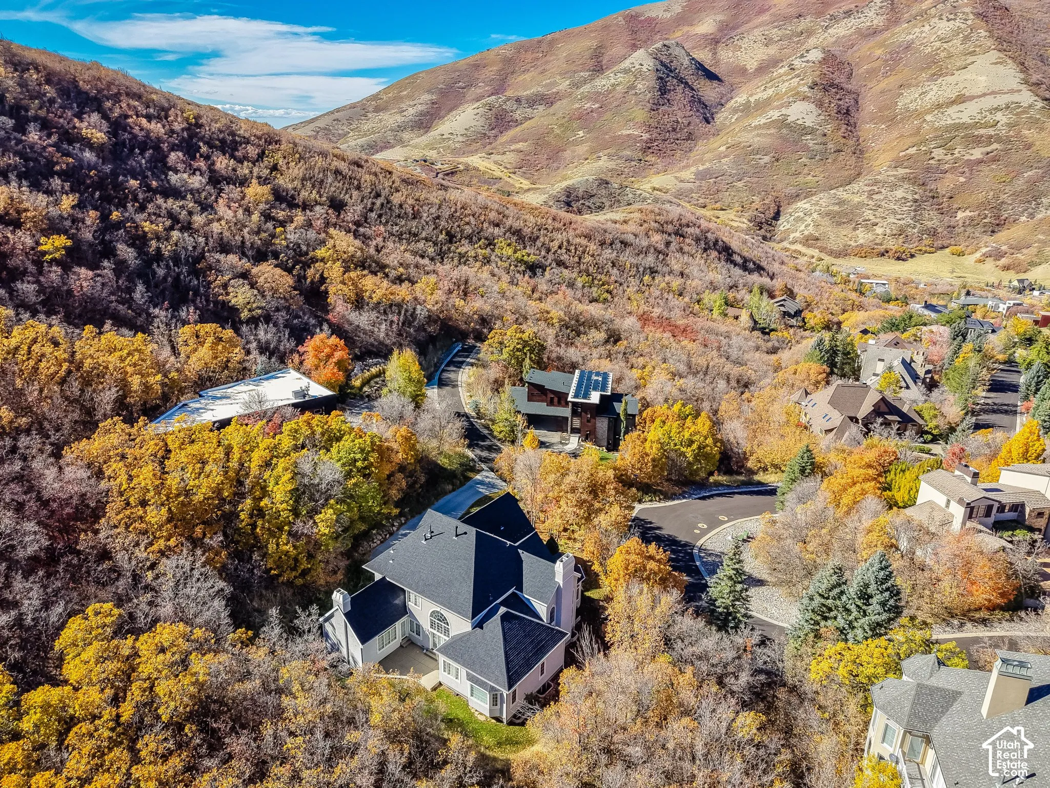 Aerial perspective featuring a multi-story residence with a high-pitched shingled roof, set against a mountainous backdrop with mature deciduous trees