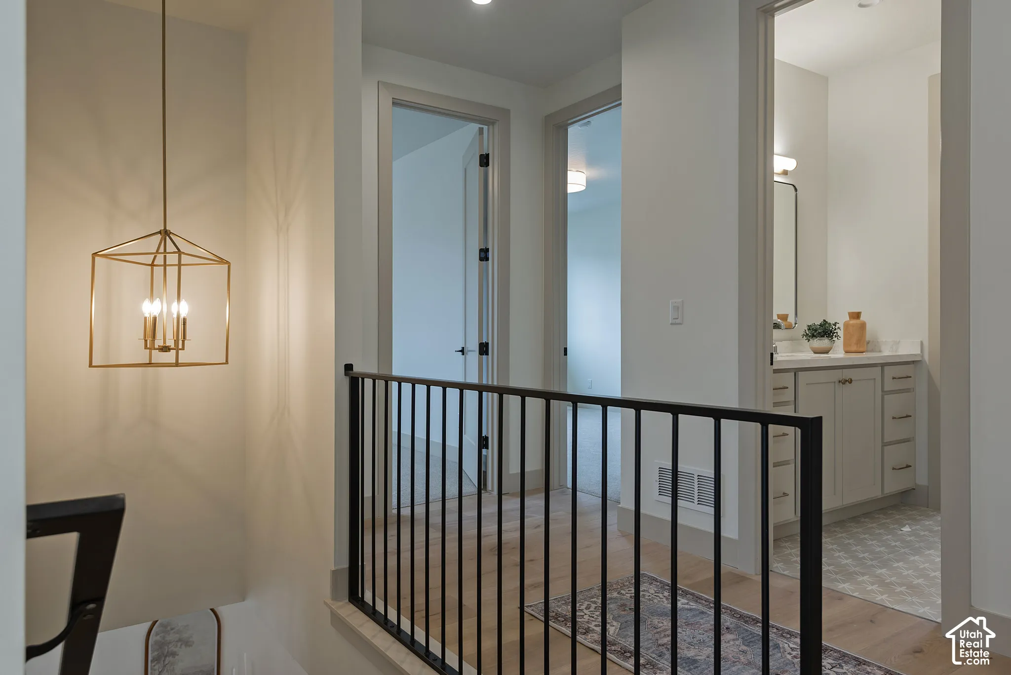 Hallway featuring wood-finish flooring, a geometric gold-tone pendant light fixture, a black metal railing, and a vanity with white cabinetry and a solid-surface countertop