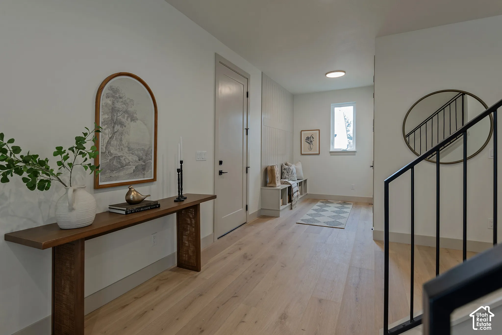 Entryway featuring light-toned wood-finish flooring, built-in mudroom bench with shelving, vertical panel wall detailing, and a black metal staircase railing