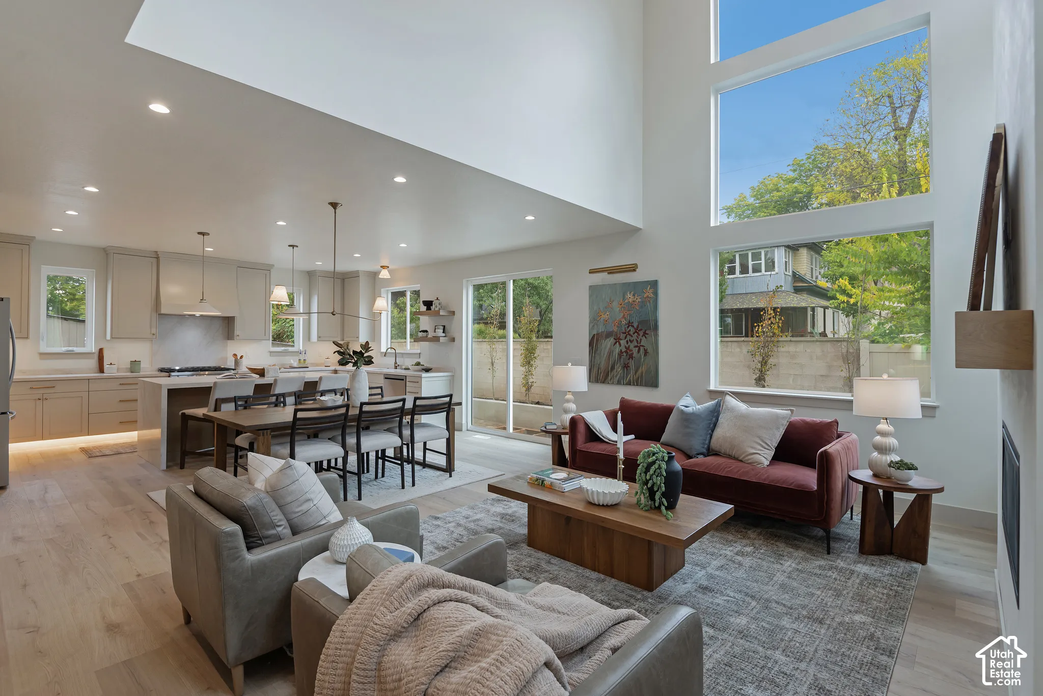 Open-concept interior featuring vaulted ceilings, floor-to-ceiling windows, wood-finish flooring, recessed lighting, and cabinetry with under-cabinet lighting