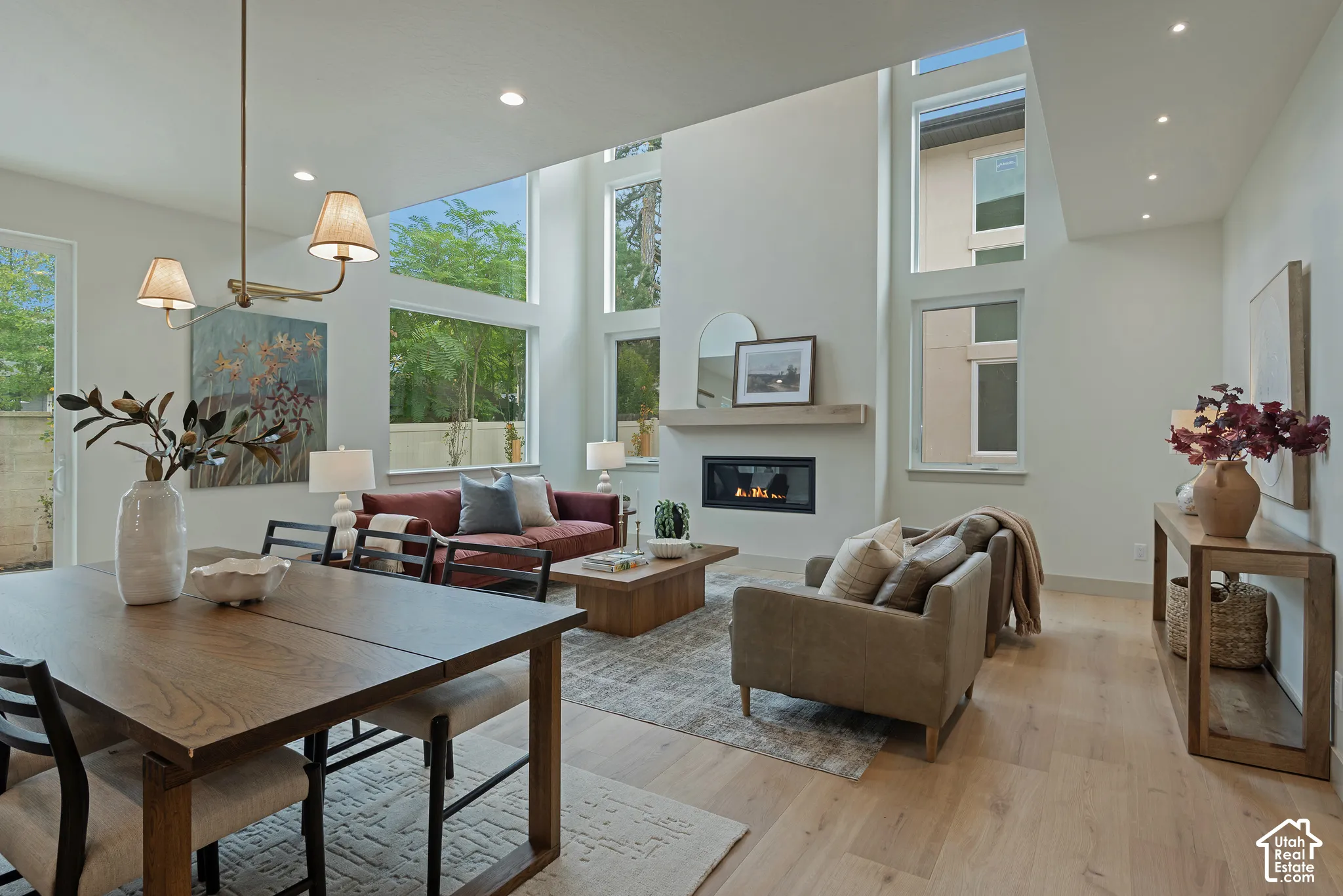 Vaulted ceilings with double-height windows, floor-to-ceiling fireplace with a wood mantel, and wood-finish flooring