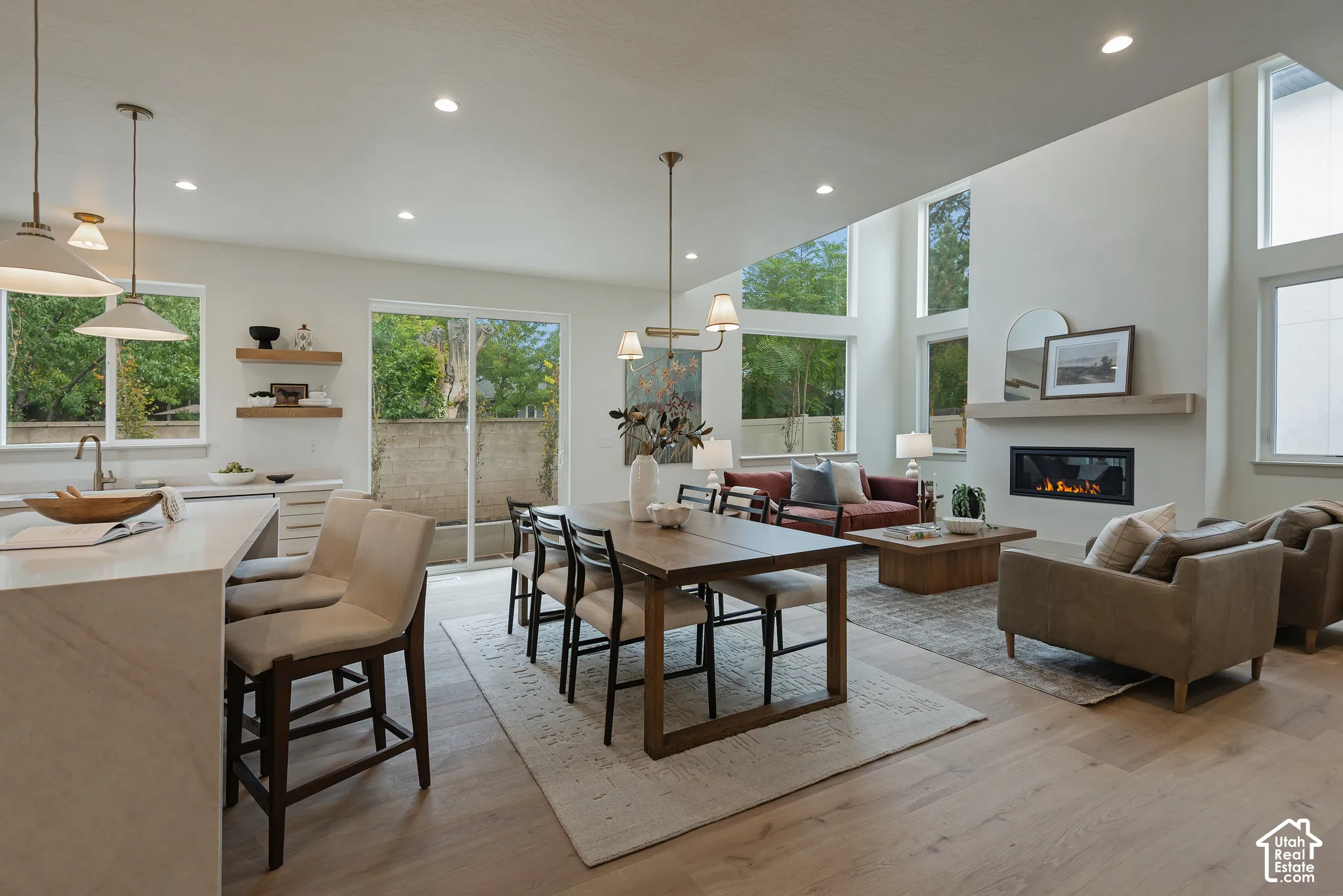 Open-concept living space featuring wood-finish flooring, soaring ceilings, a linear fireplace with a natural wood mantel, floor-to-ceiling windows, and recessed lighting