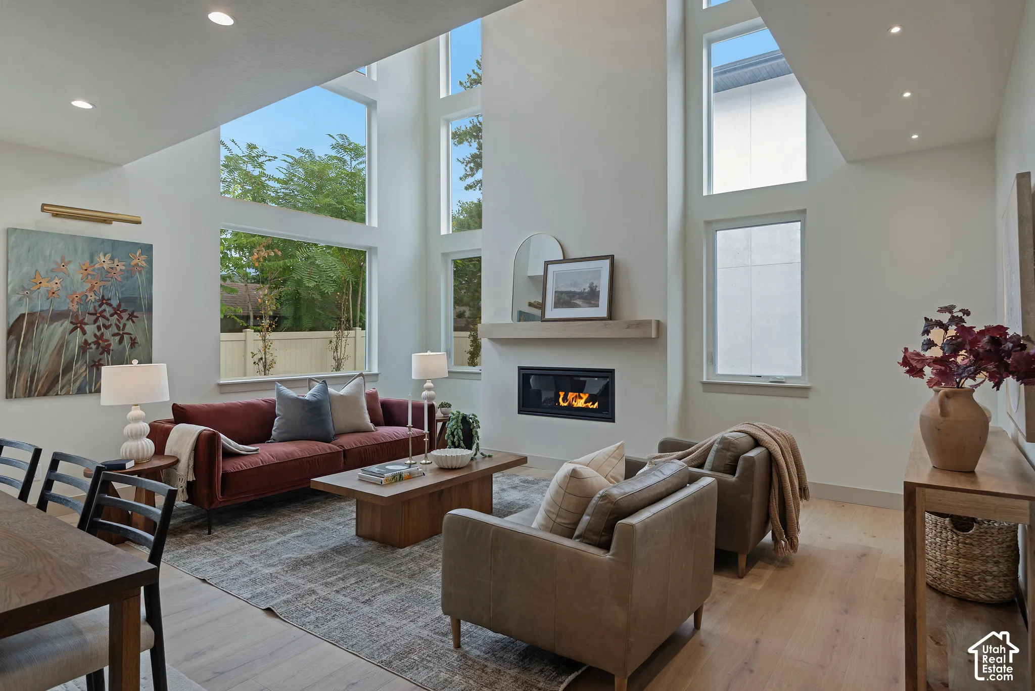 Double-height ceilings, floor-to-ceiling windows, linear gas fireplace with a wood mantel, recessed lighting, and wood-finish flooring