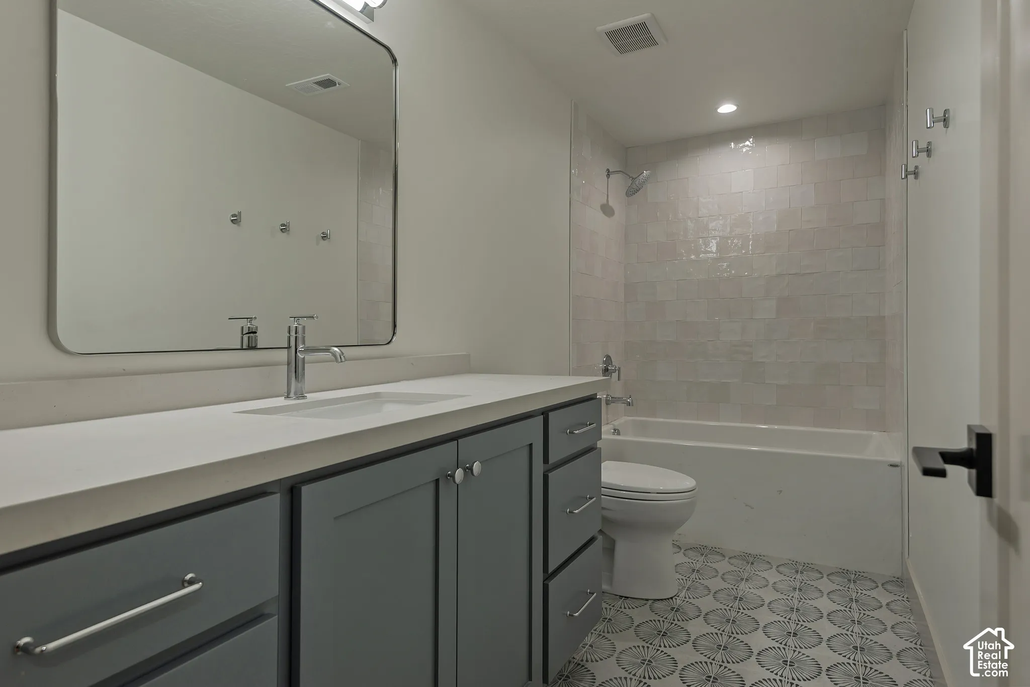 Bathroom featuring blue cabinetry, a light-toned countertop with an integrated sink, a rectangular mirror with rounded edges, a tub-shower combination with textured wall tile, and patterned tile flooring