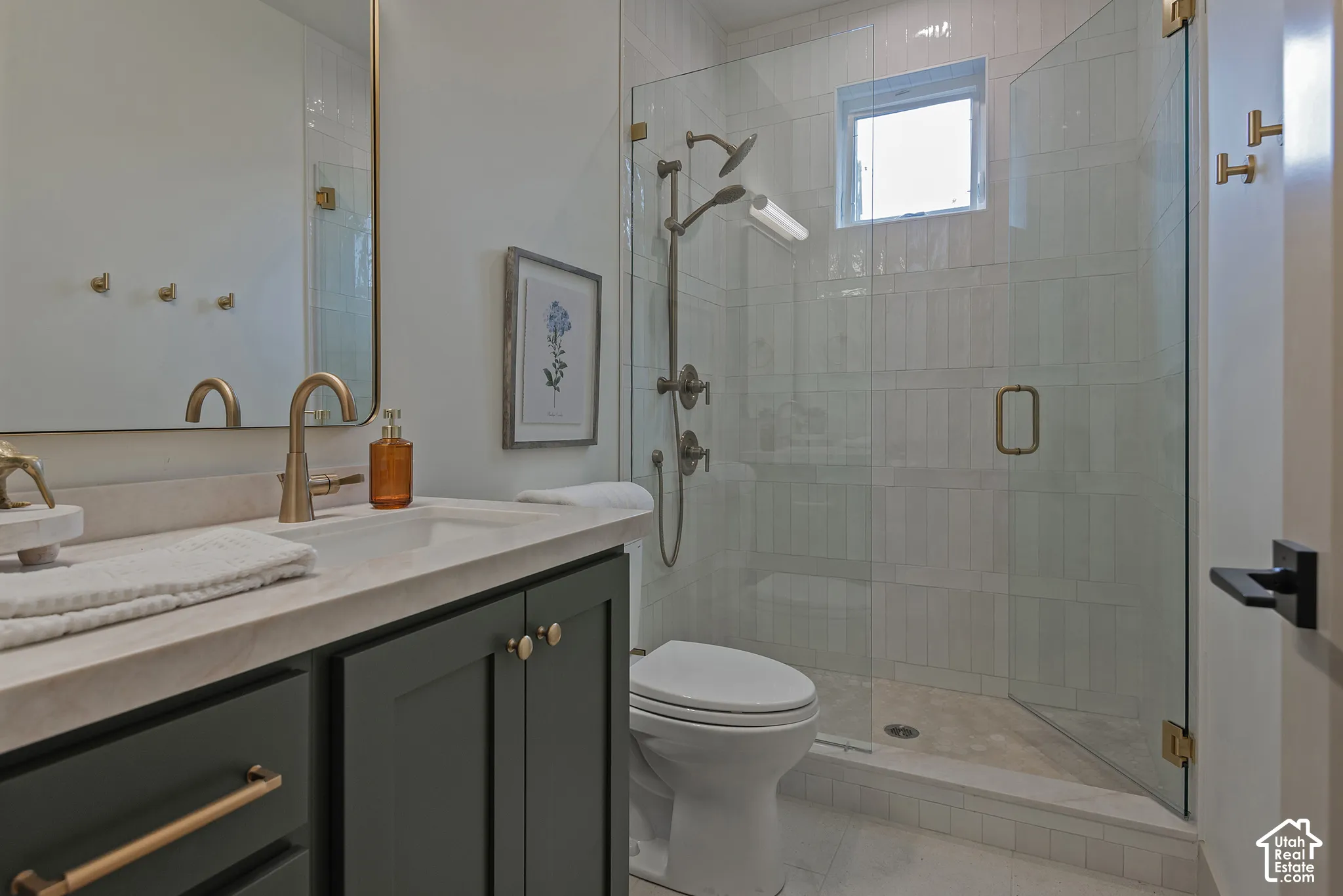 Dark-finish vanity with a stone countertop, brass-toned fixtures, rectangular wall-mounted mirror, and a walk-in shower featuring glass paneling and wall-mounted plumbing hardware