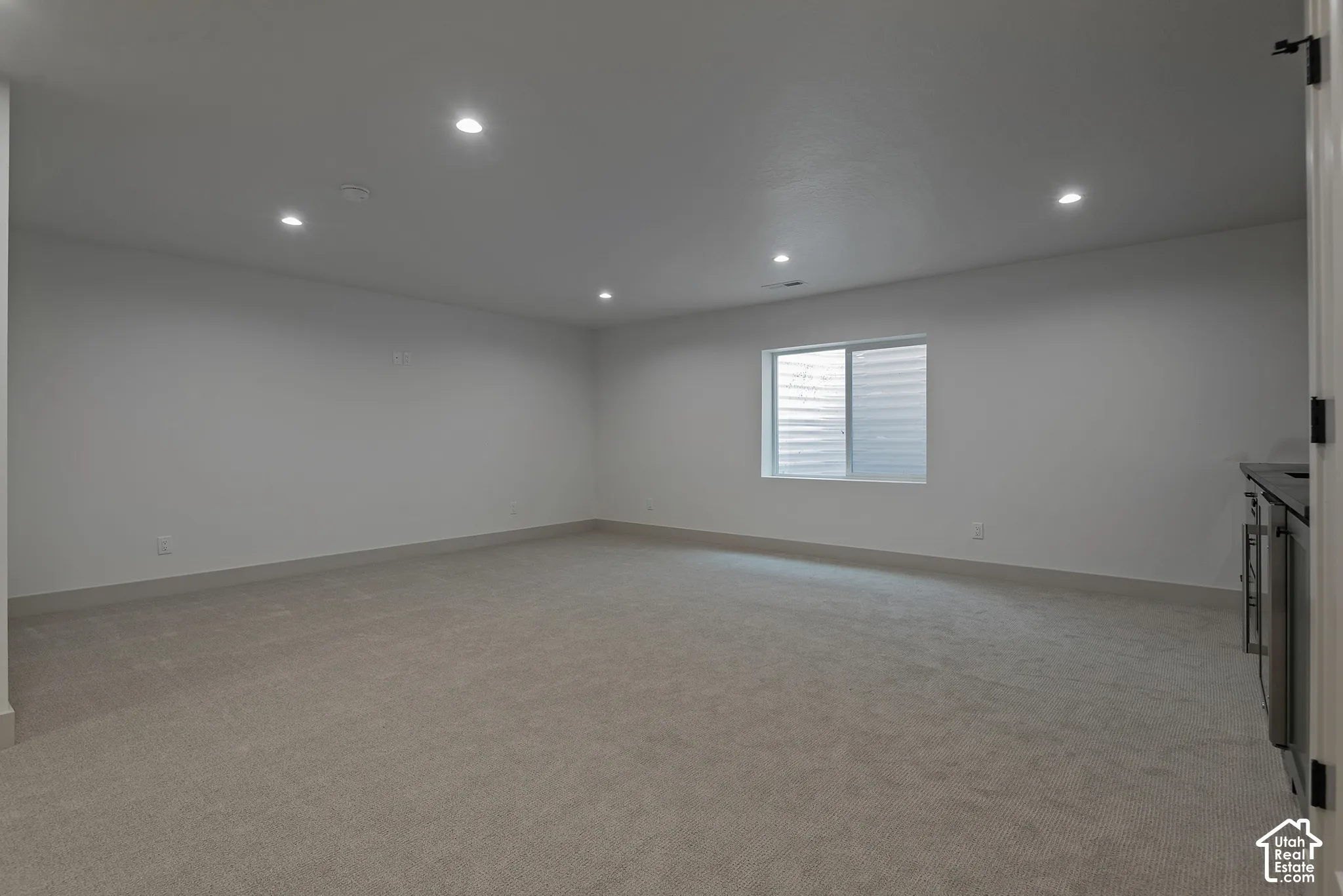 Expansive room featuring neutral wall-to-wall carpeting, recessed ceiling lighting, and a single window with horizontal blinds