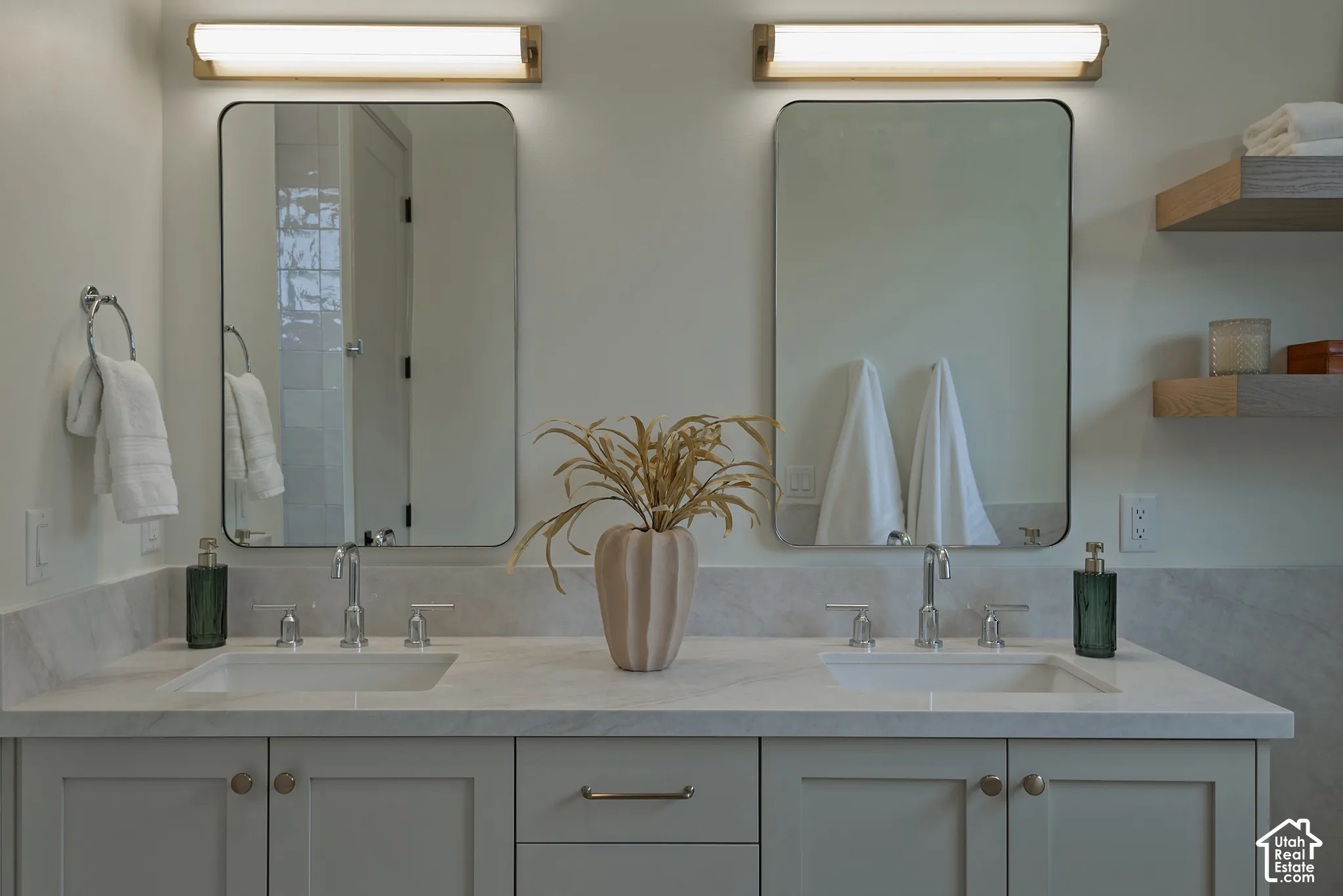 Double vanity featuring a stone countertop, dual undermount sinks, rectangular mirrors with rounded corners, wall-mounted linear light fixtures, and built-in floating shelves