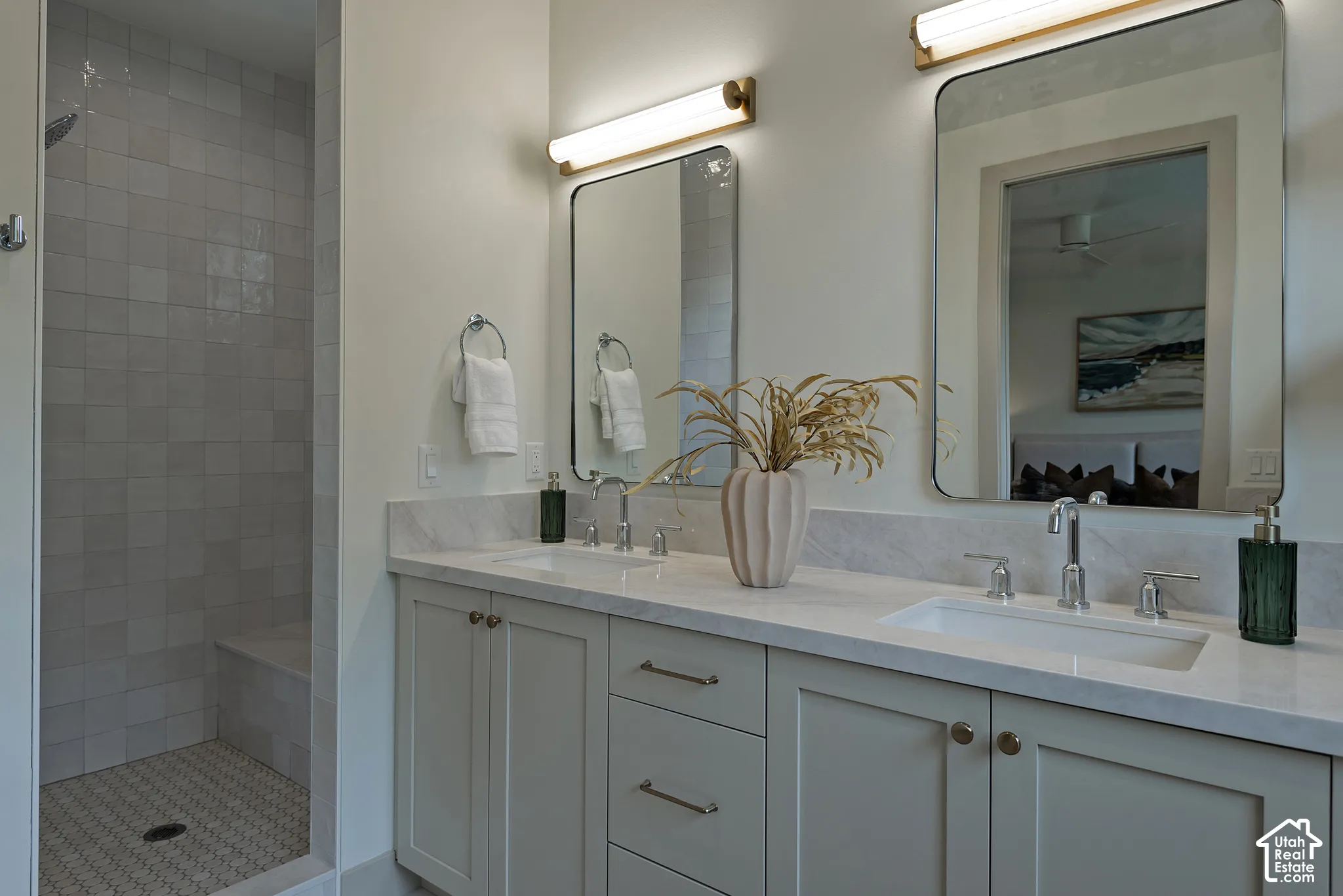 Dual-vanity cabinetry with stone-finish countertops, undermount sinks, wall-mounted linear lighting, and dual rounded-corner mirrors, paired with a walk-in shower featuring tiled walls and a built-in bench