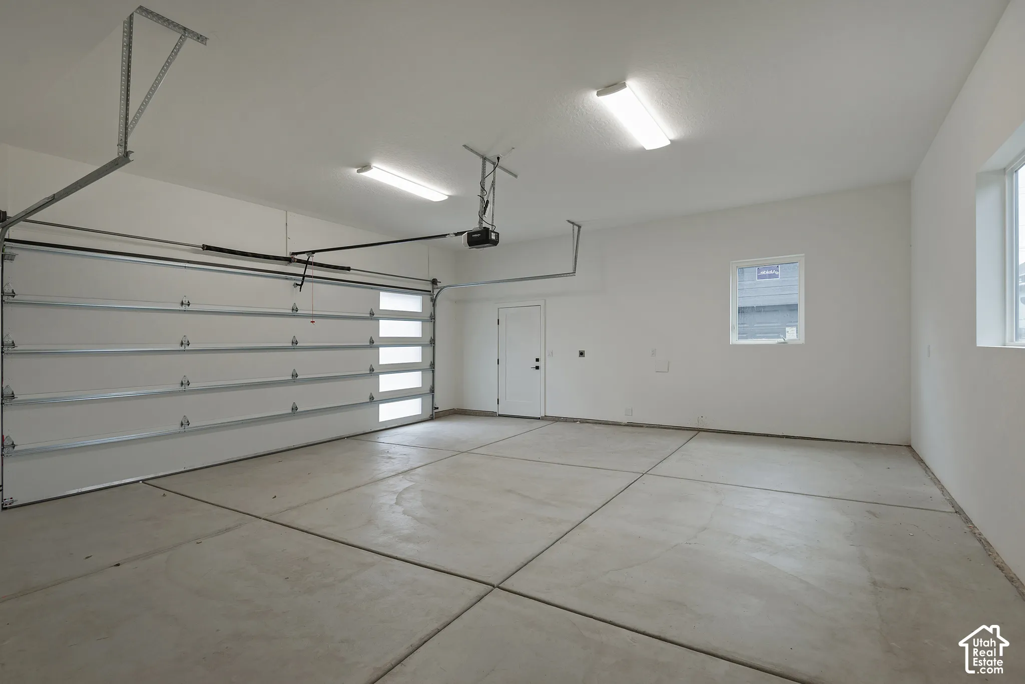 Attached garage featuring a concrete floor with expansion joints, dual overhead fluorescent lighting, a sectional garage door with opaque glass panels, and an exterior access door
