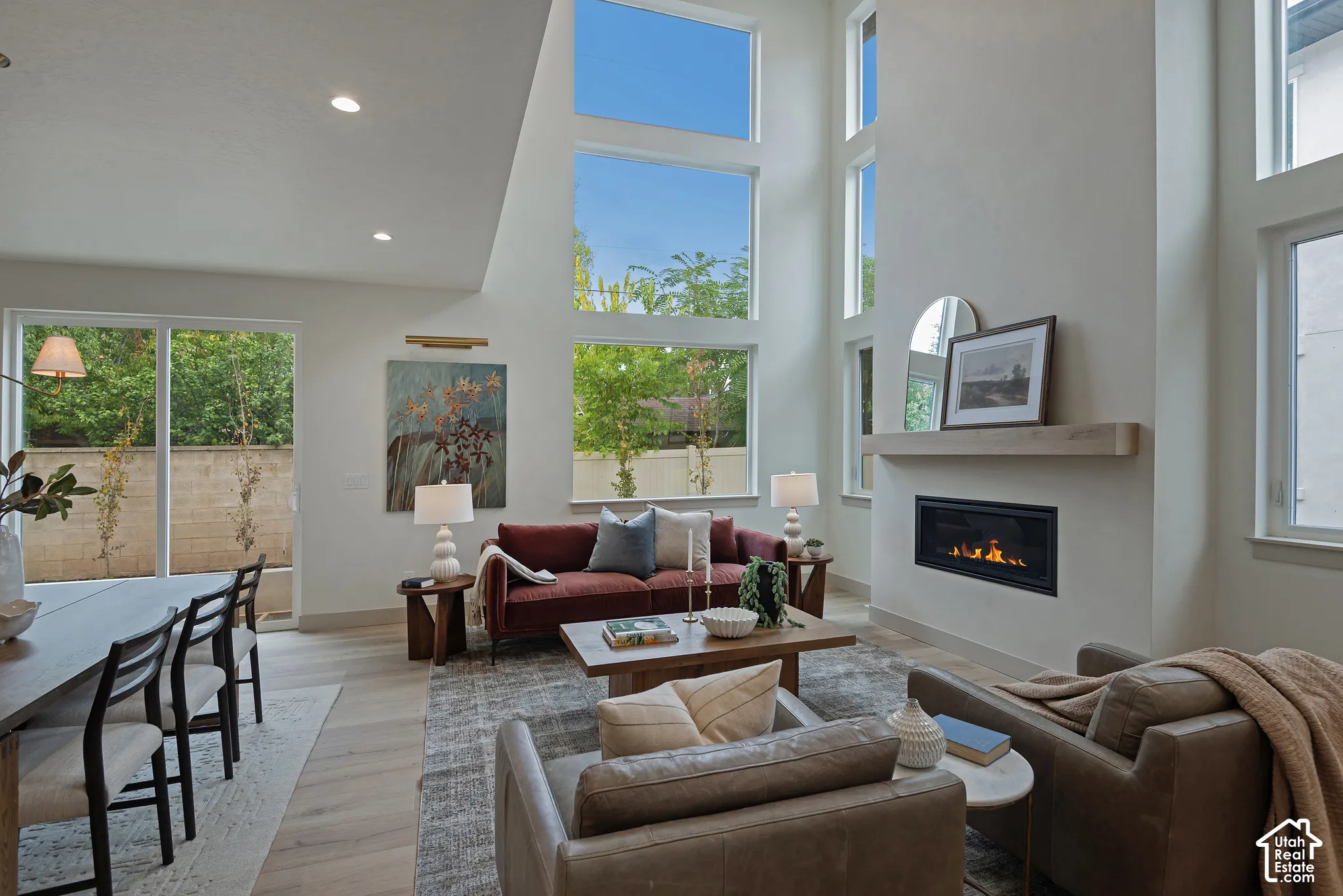 Double-height living area featuring floor-to-ceiling windows, wood-finish flooring, recessed lighting, and a linear gas fireplace with a wood-beam mantel
