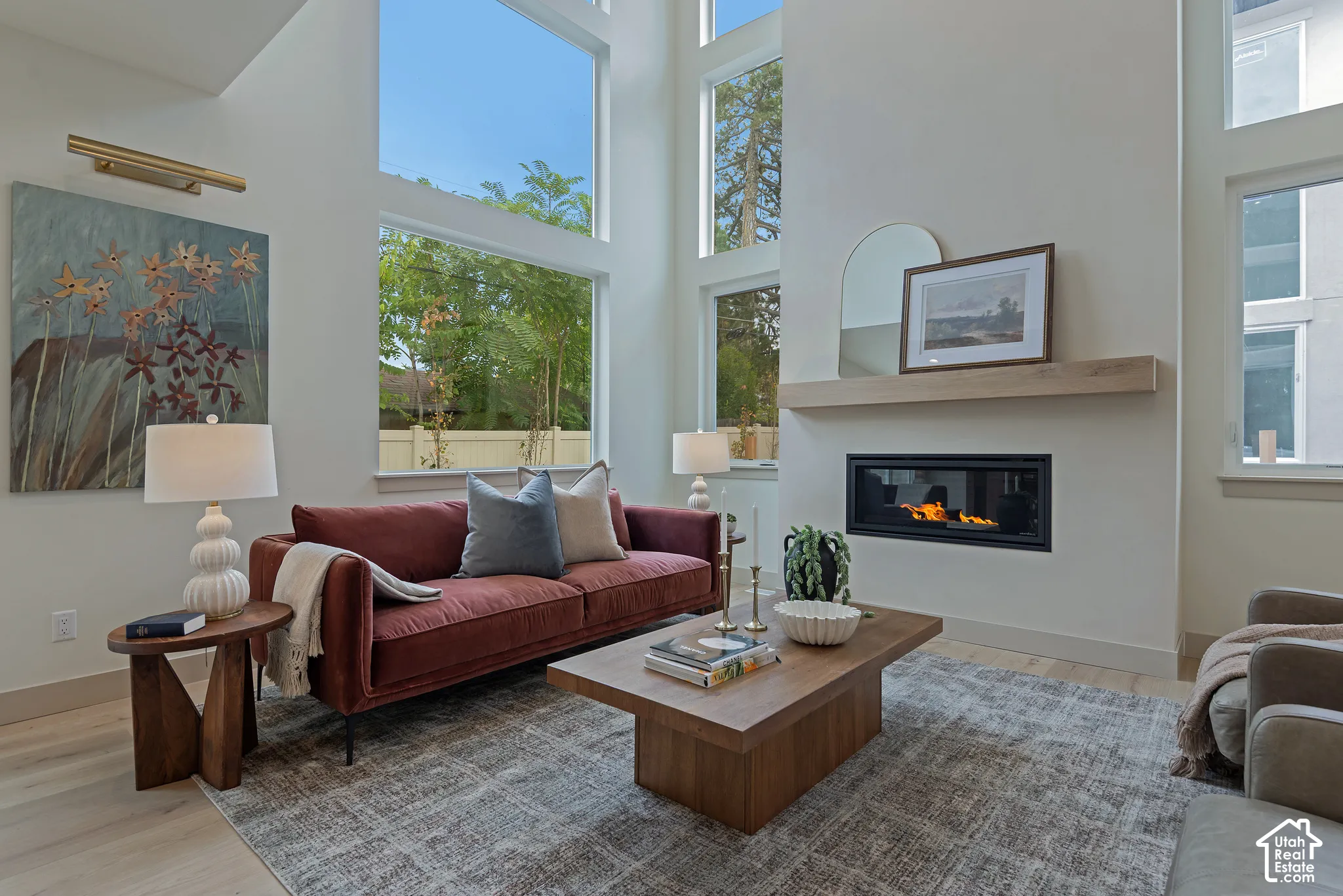Double-height ceilings featuring floor-to-ceiling windows, linear built-in fireplace, and natural wood floating mantel